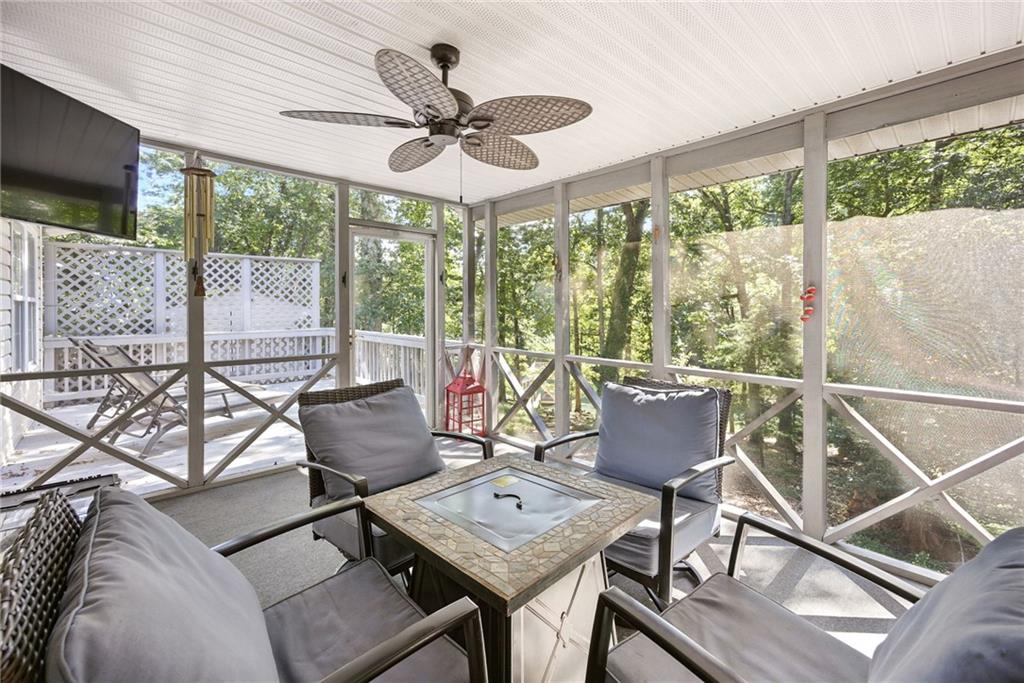 Screened porch with cushioned seating, a ceiling fan, and leafy tree views.