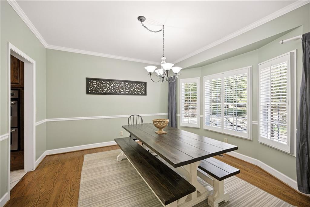 Dining room with a dark wood table and benches beneath a chandelier, beside windows with white plantation shutters.