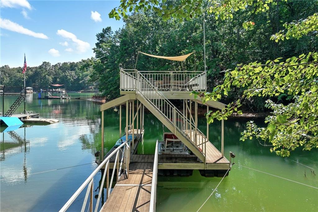 Wooden lake dock with a raised deck and stairs over calm, tree-lined water.