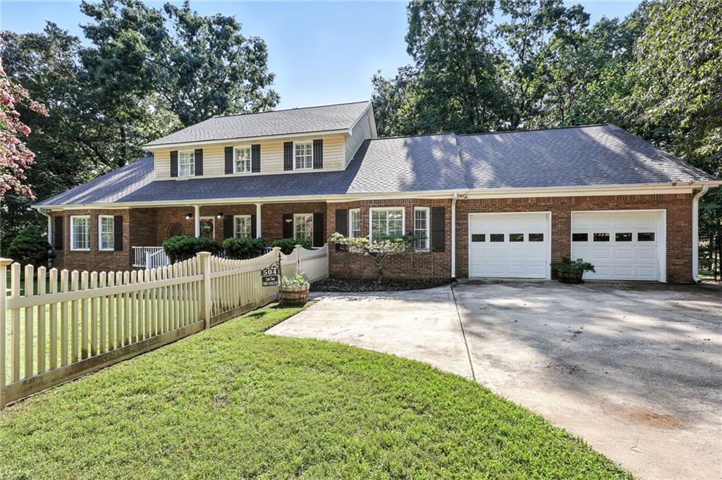 Red-brick house with a raised dormer, two garage doors, and a white picket fence.