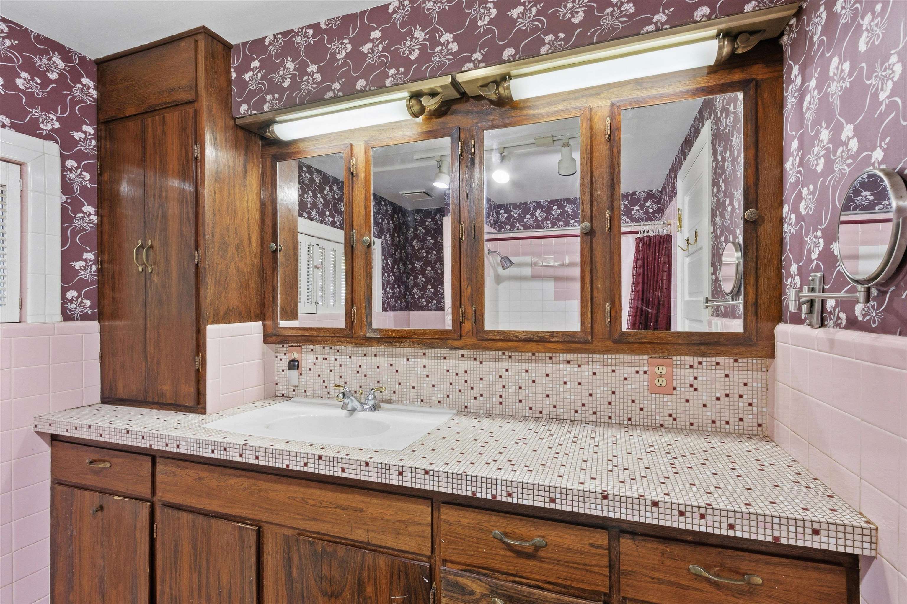Bathroom vanity with mosaic tile countertop, dark wood cabinetry, and mauve floral wallpaper.