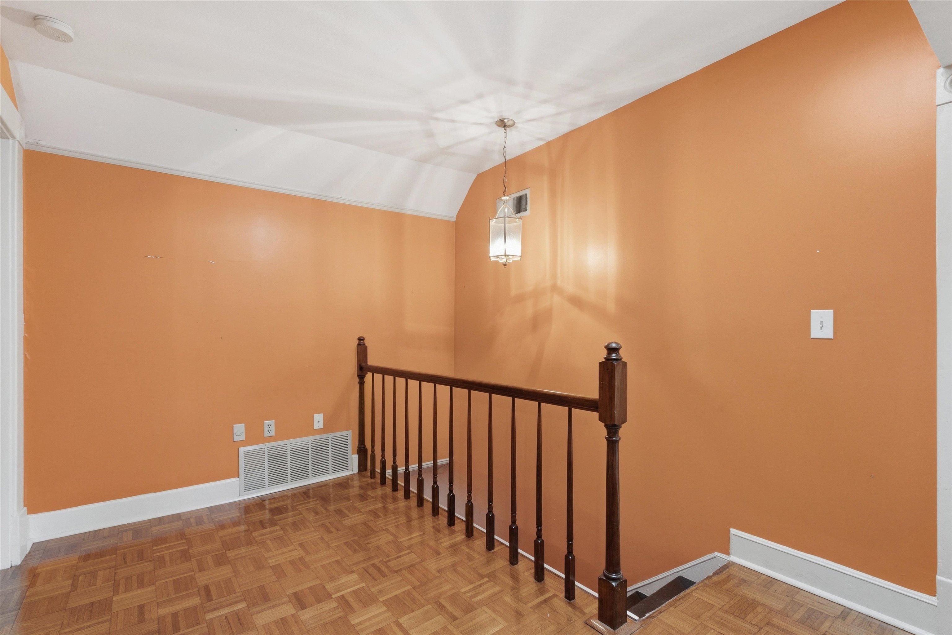 Upstairs landing with orange walls, parquet flooring, and a dark wooden stair railing.