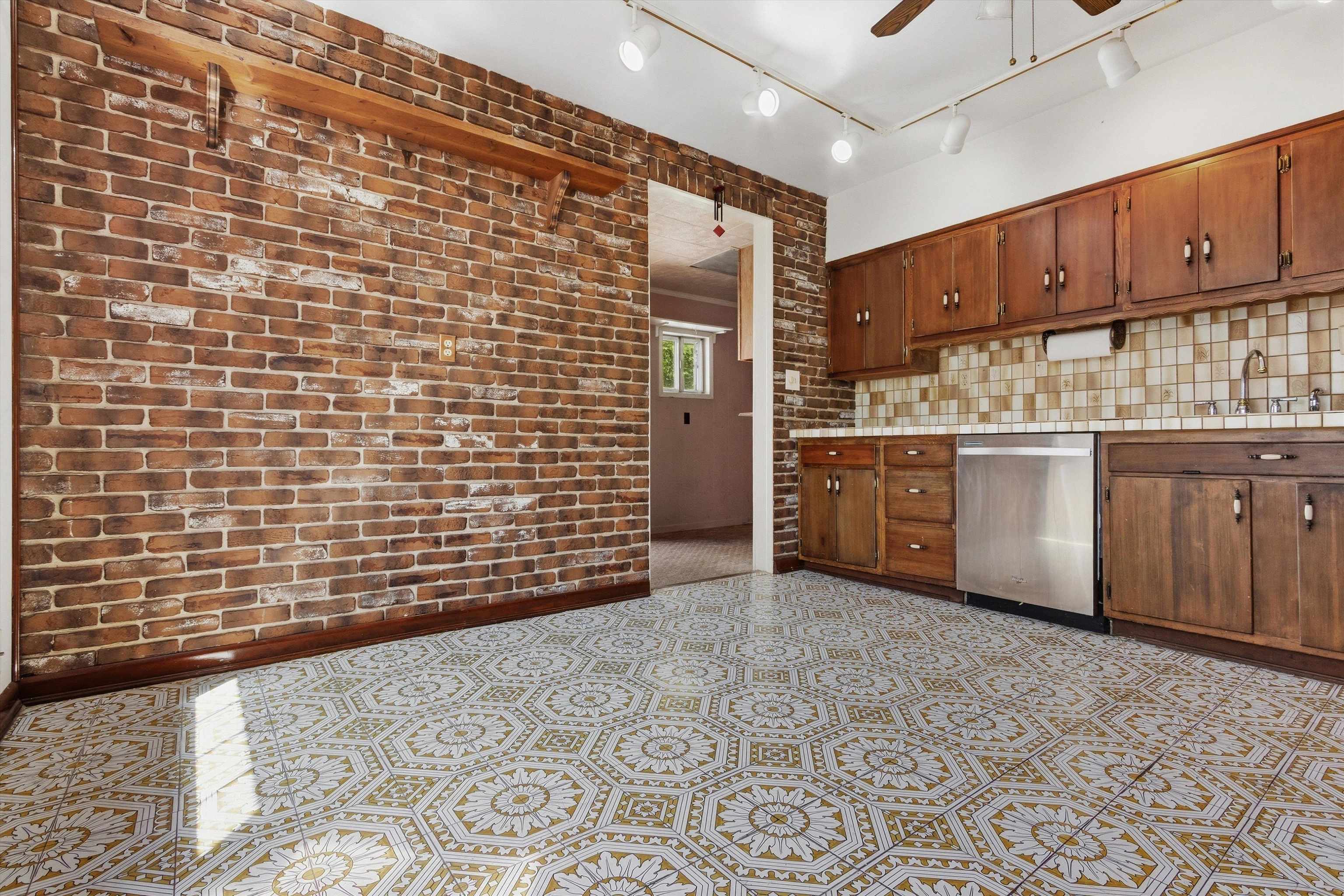 Kitchen with an exposed brick wall, wood cabinets, and ornate patterned tile flooring.