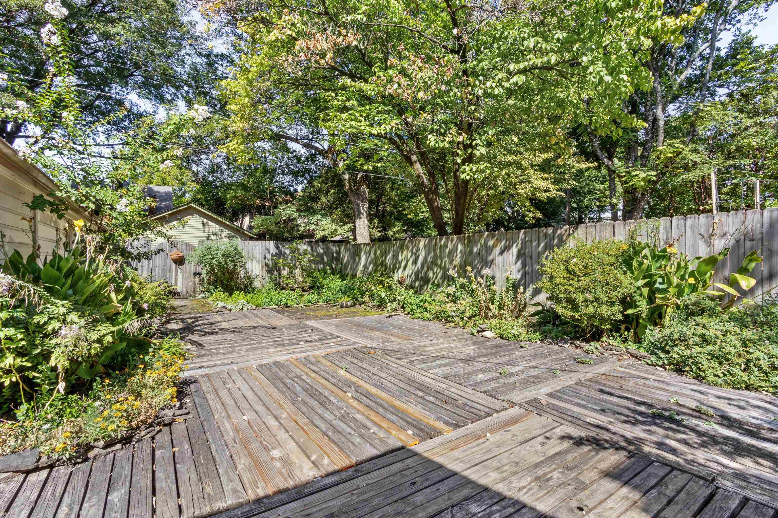 Wooden backyard deck surrounded by garden beds and mature trees, enclosed by a tall privacy fence.