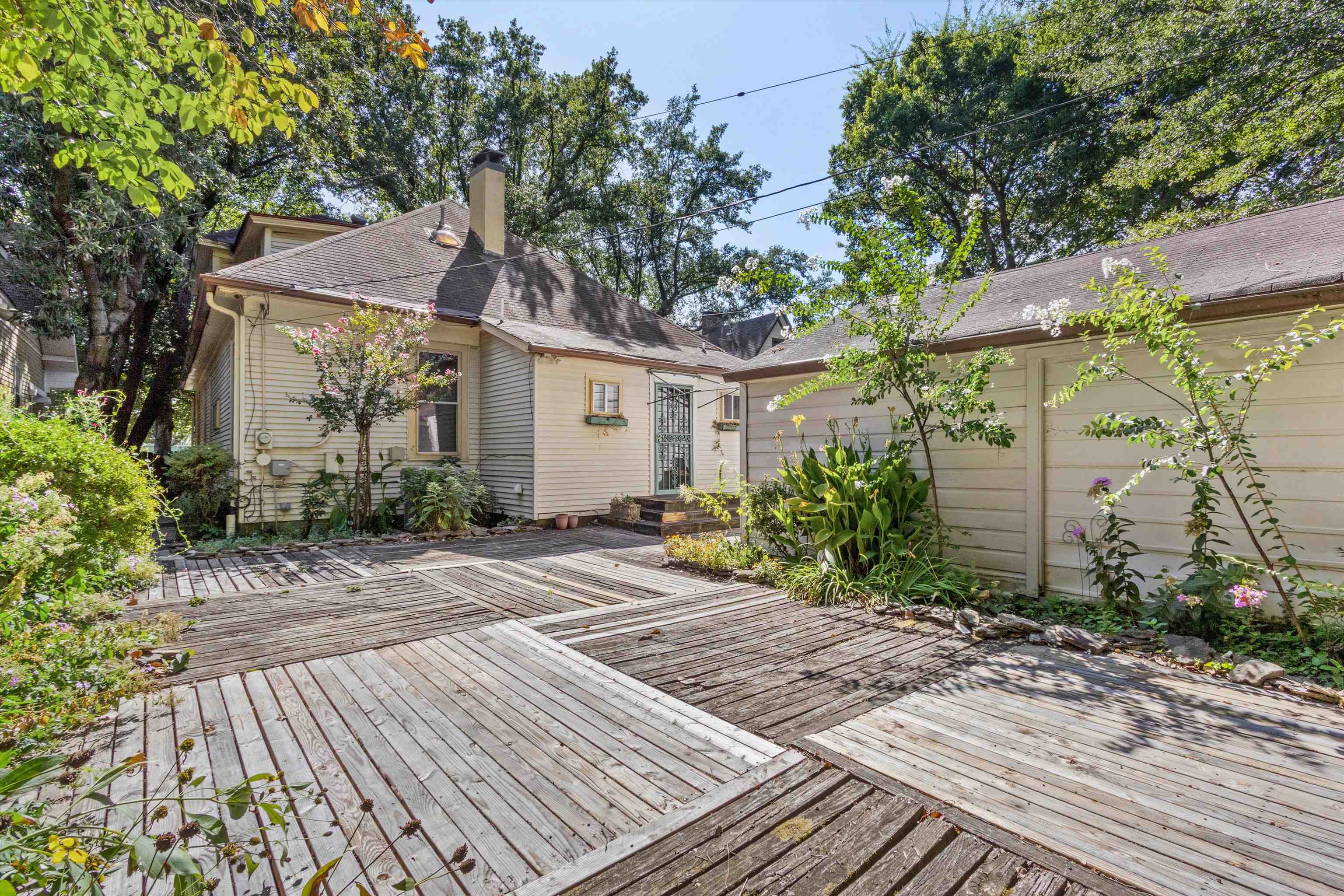 House rear exterior with a wide wooden deck and leafy garden plantings.