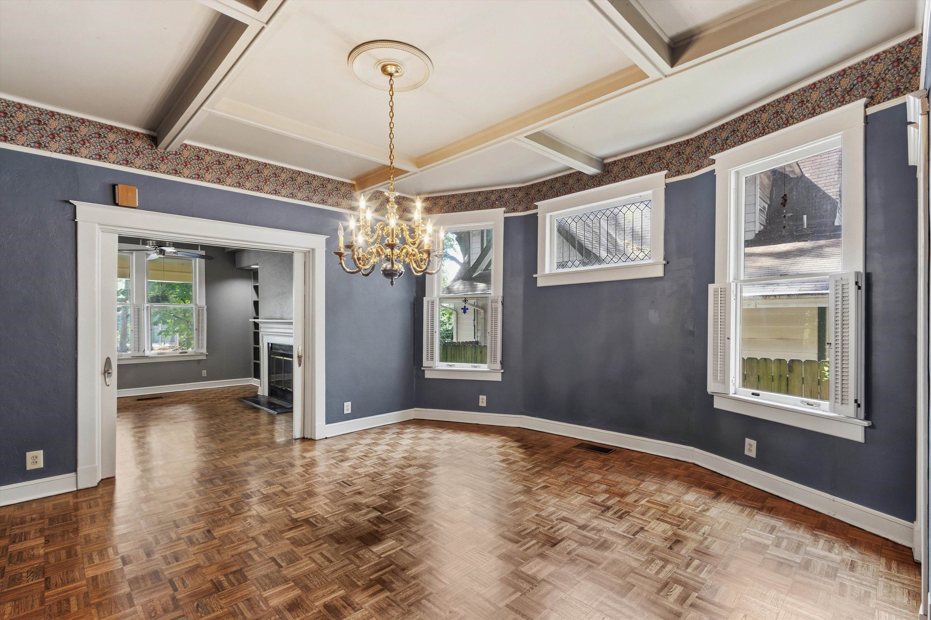 Empty dining room with parquet flooring, shuttered windows, and a brass chandelier.