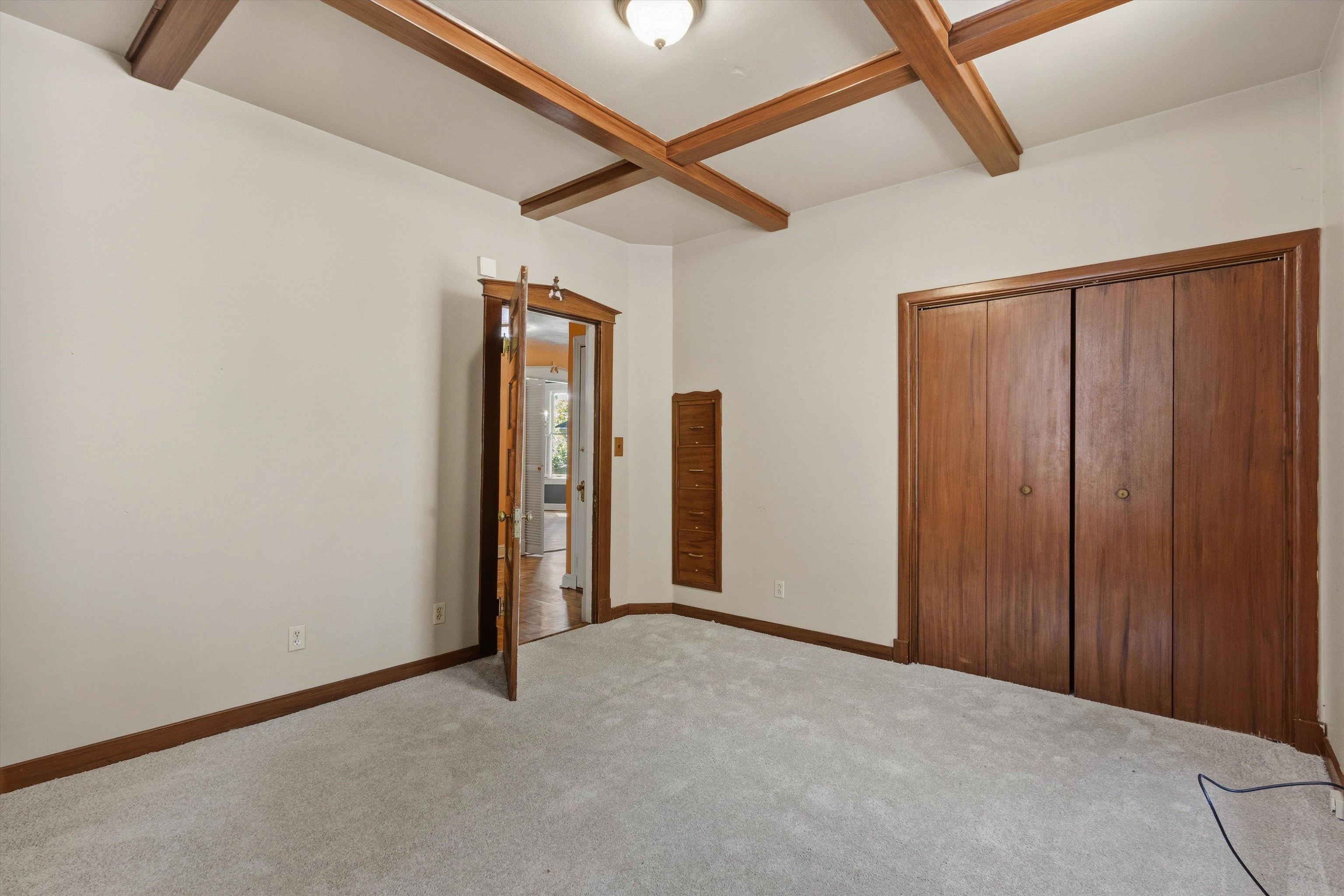 Empty bedroom with exposed wooden ceiling beams and built-in wooden storage.