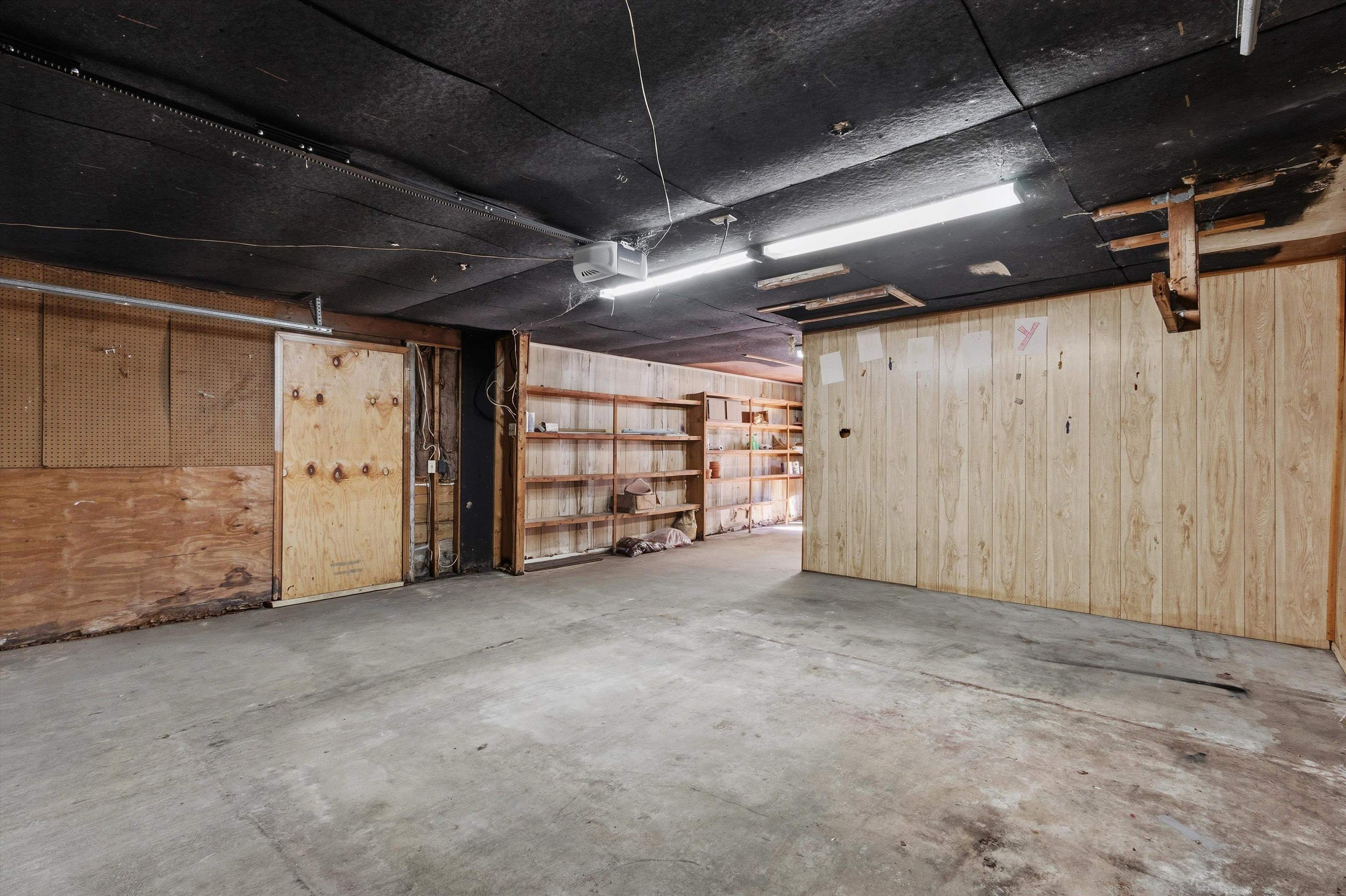 Unfinished garage with concrete floor, plywood walls, and built-in shelving.