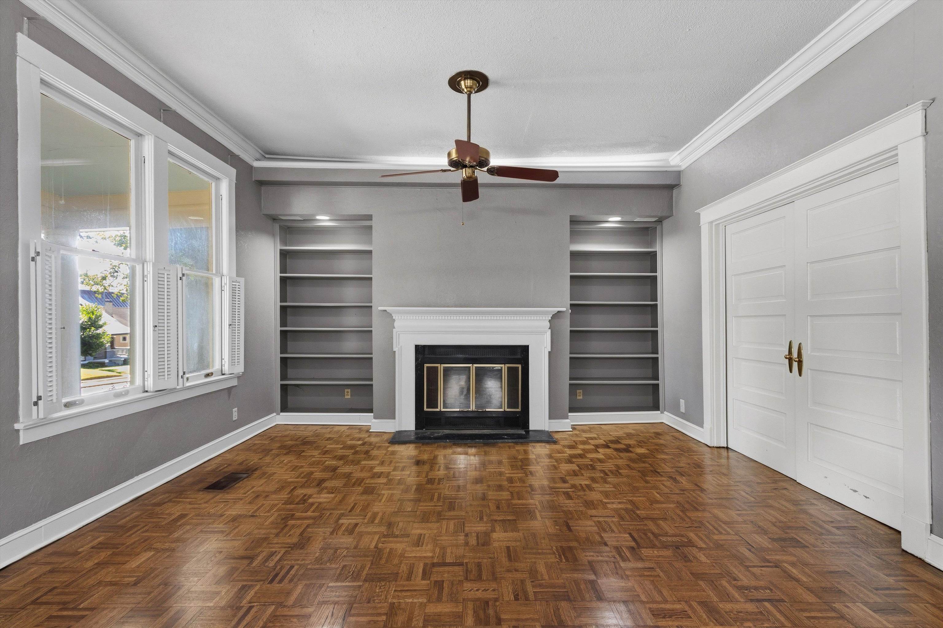 Vacant living room with a white fireplace, built-in bookshelves, and parquet flooring.