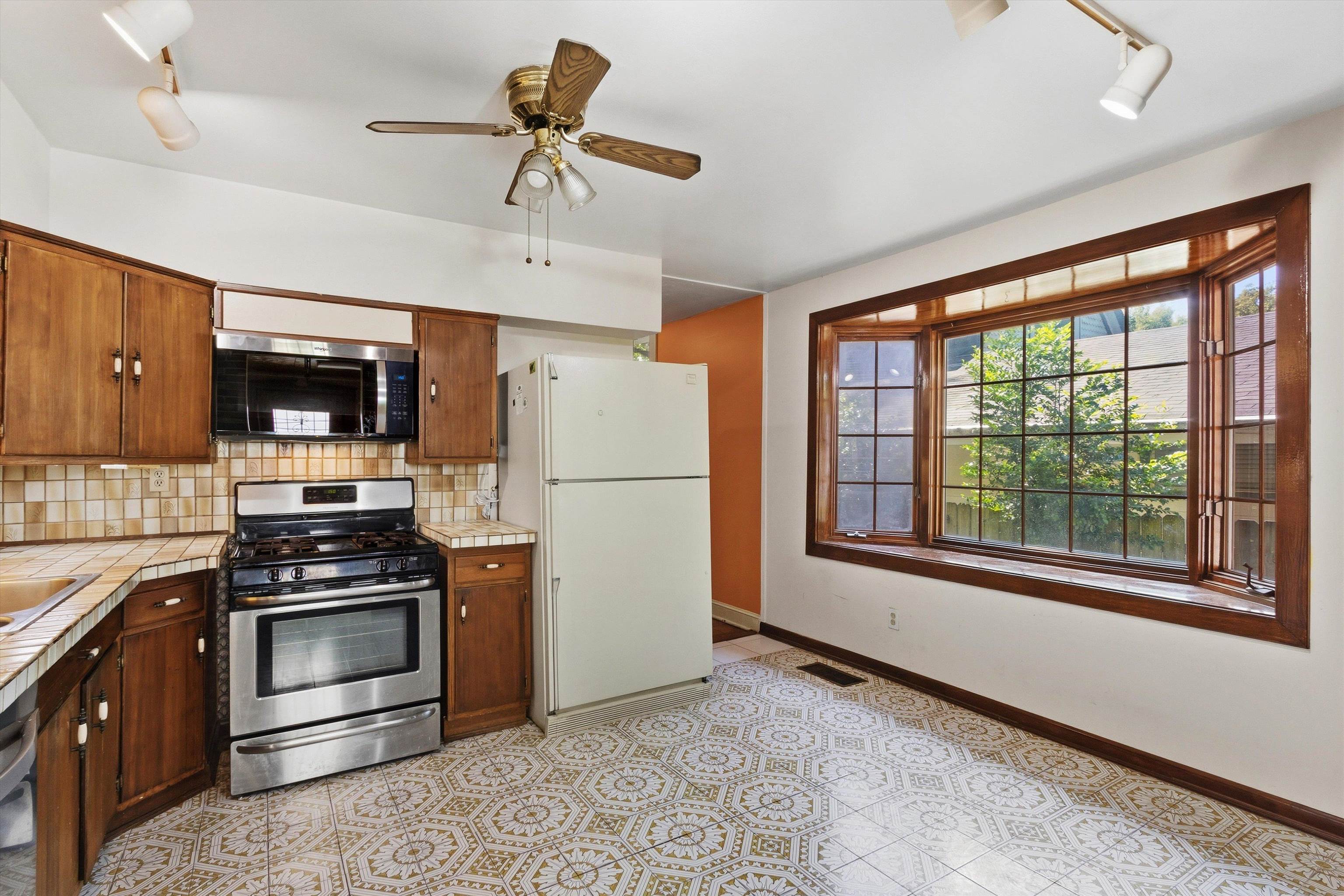 Kitchen with dark wood cabinets, patterned tile floor, gas range, and large wood-trimmed window.