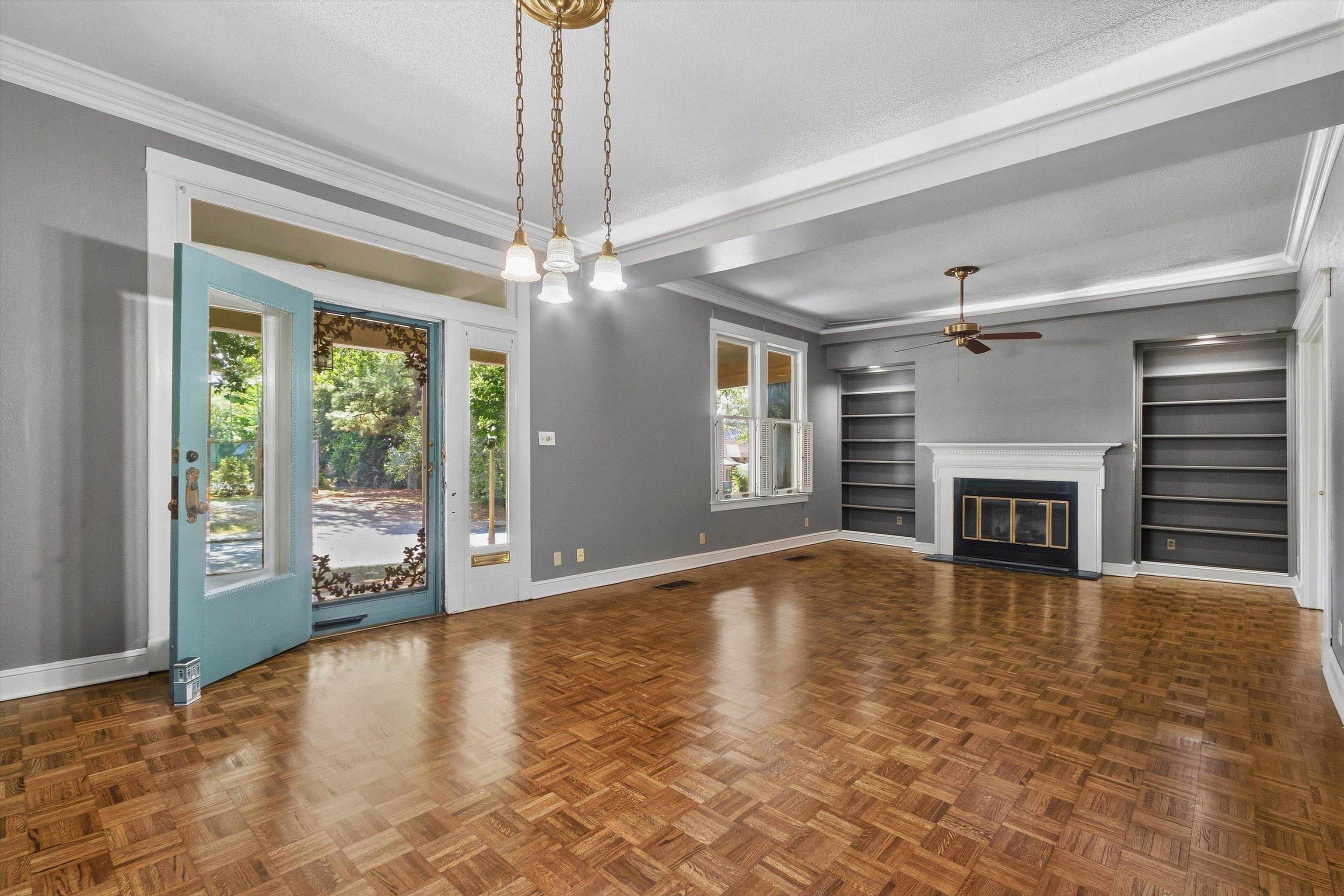 Unfurnished living room with parquet floors, an open turquoise door, built-in shelves, and a white fireplace.