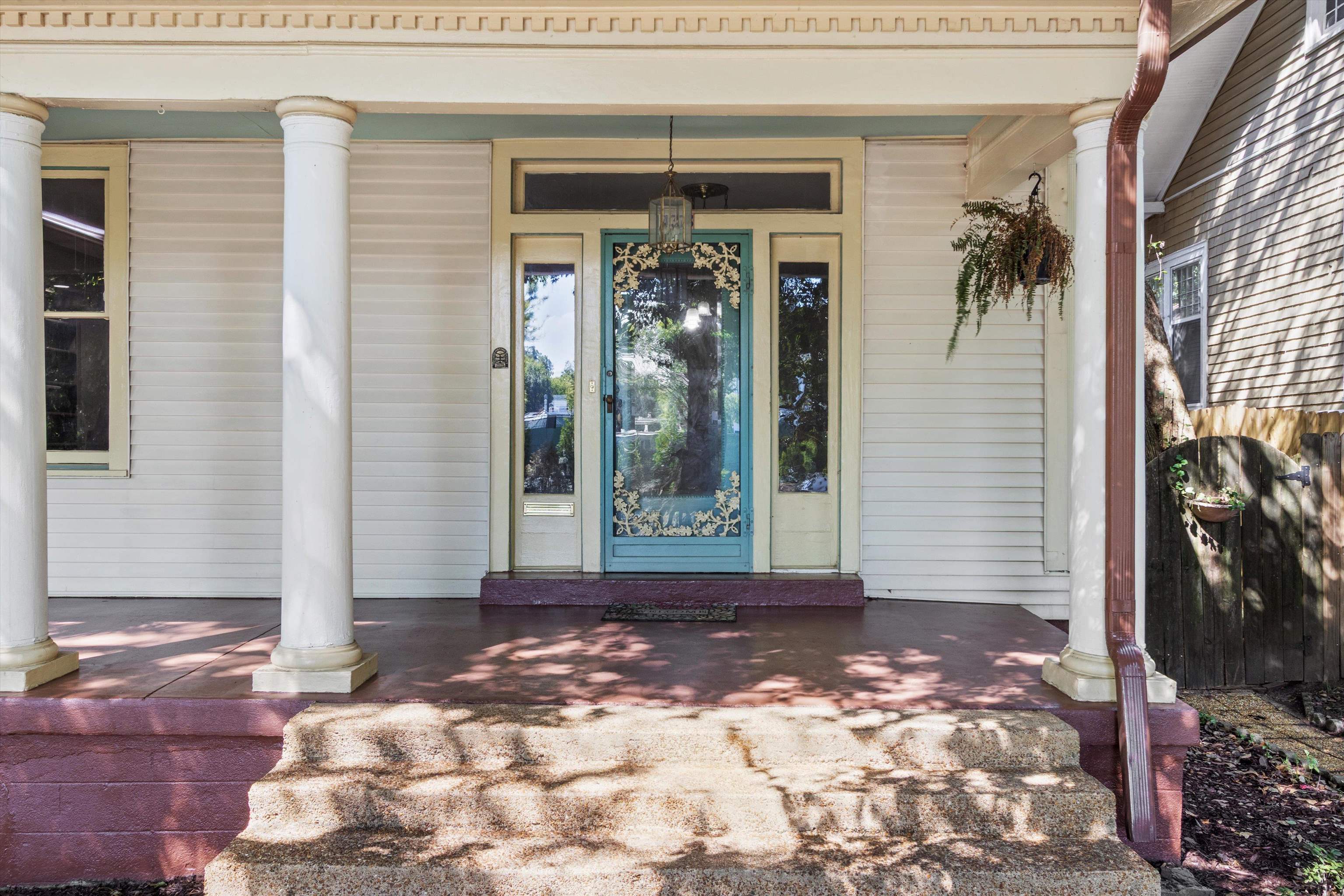 Covered front porch with white columns, broad steps, and an ornate turquoise glass door.