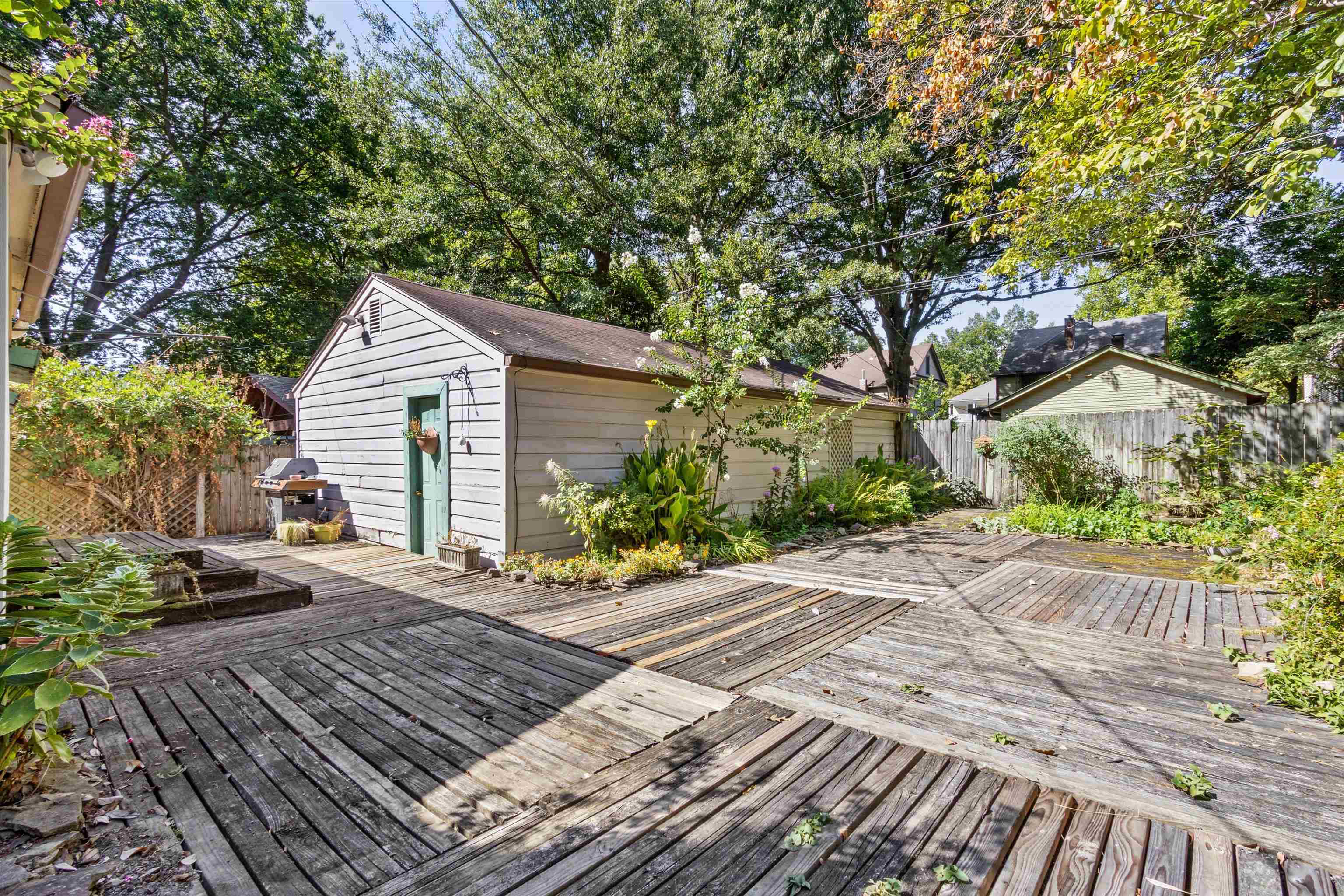Backyard deck beside a detached garage with a green door and lush garden beds.