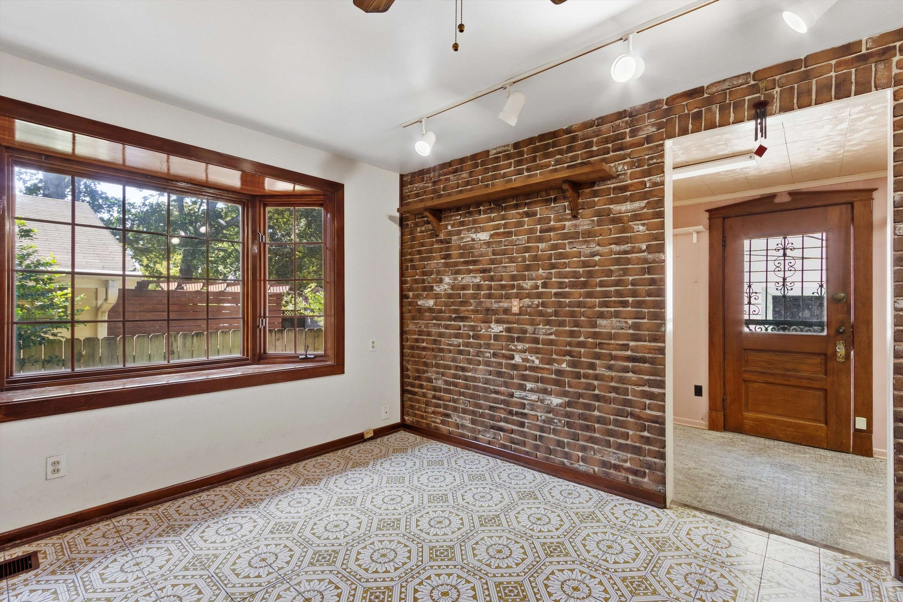Empty room with a brick accent wall, large wood-trimmed window, and ornate patterned tile floor.