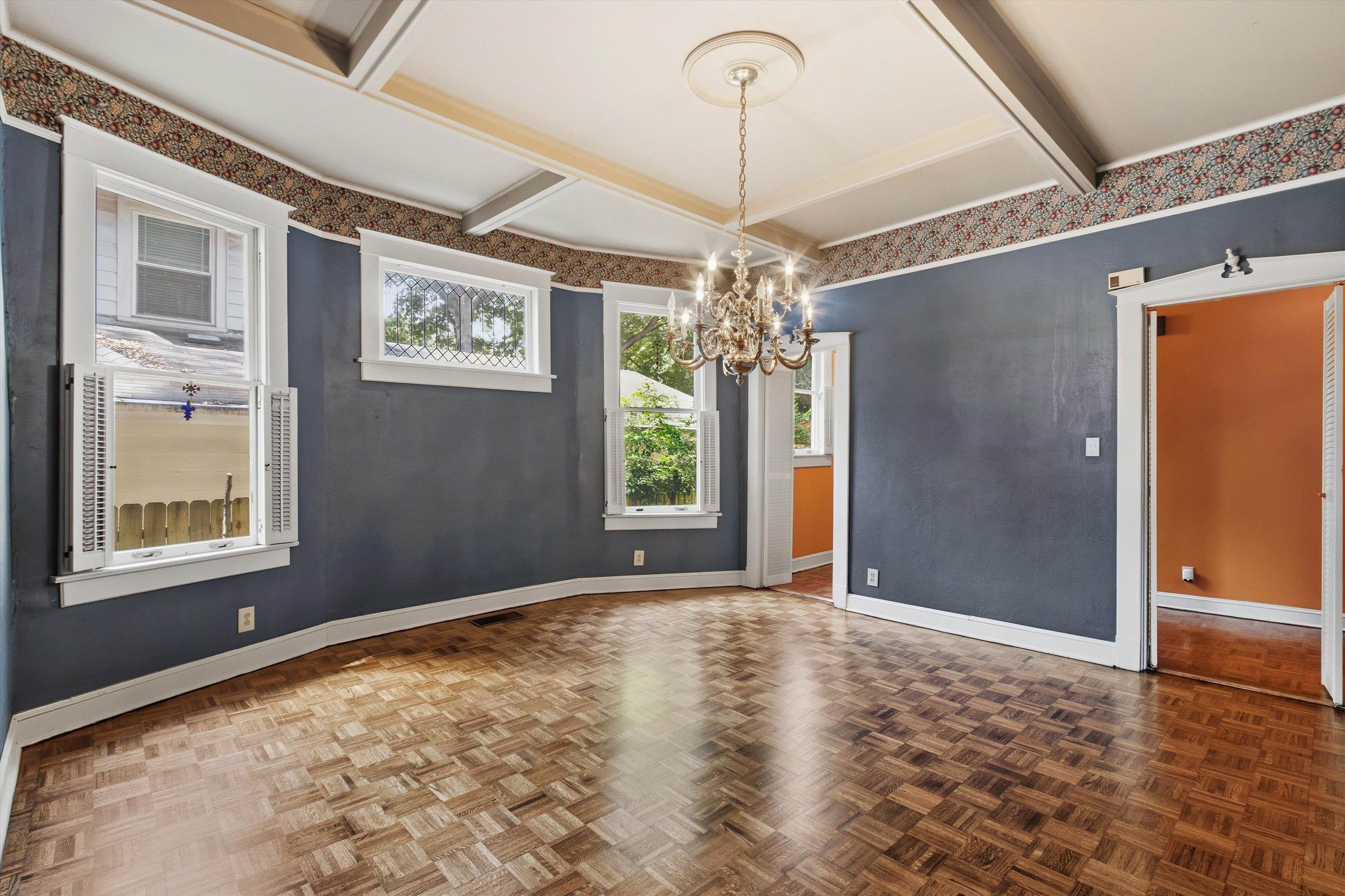 Empty blue-walled room with a chandelier, coffered ceiling, and parquet floor.