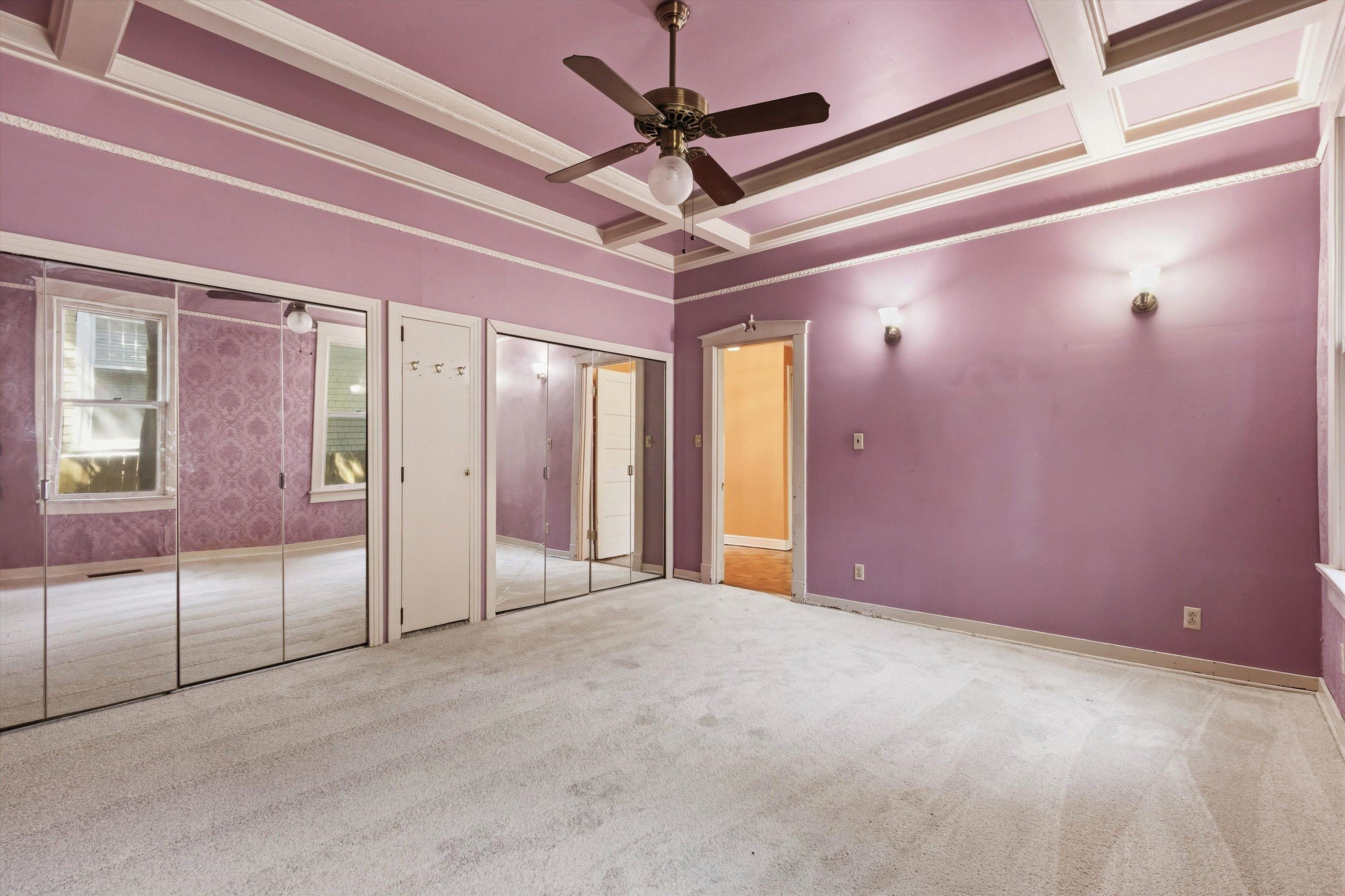 Empty mauve bedroom with a coffered ceiling, ceiling fan, and mirrored closet doors.