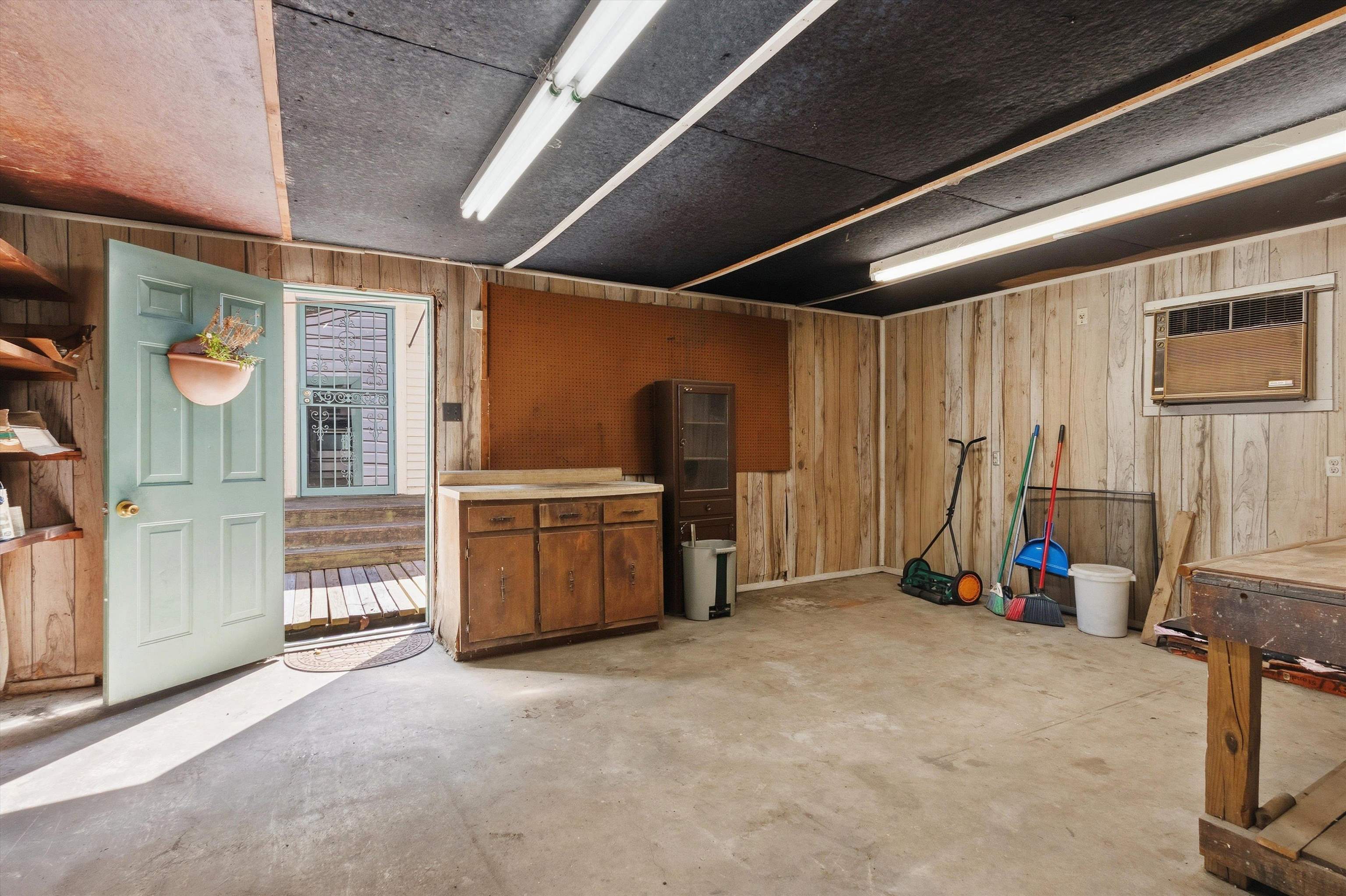 Garage with wood-paneled walls, a workbench, lawn tools, and an open door.