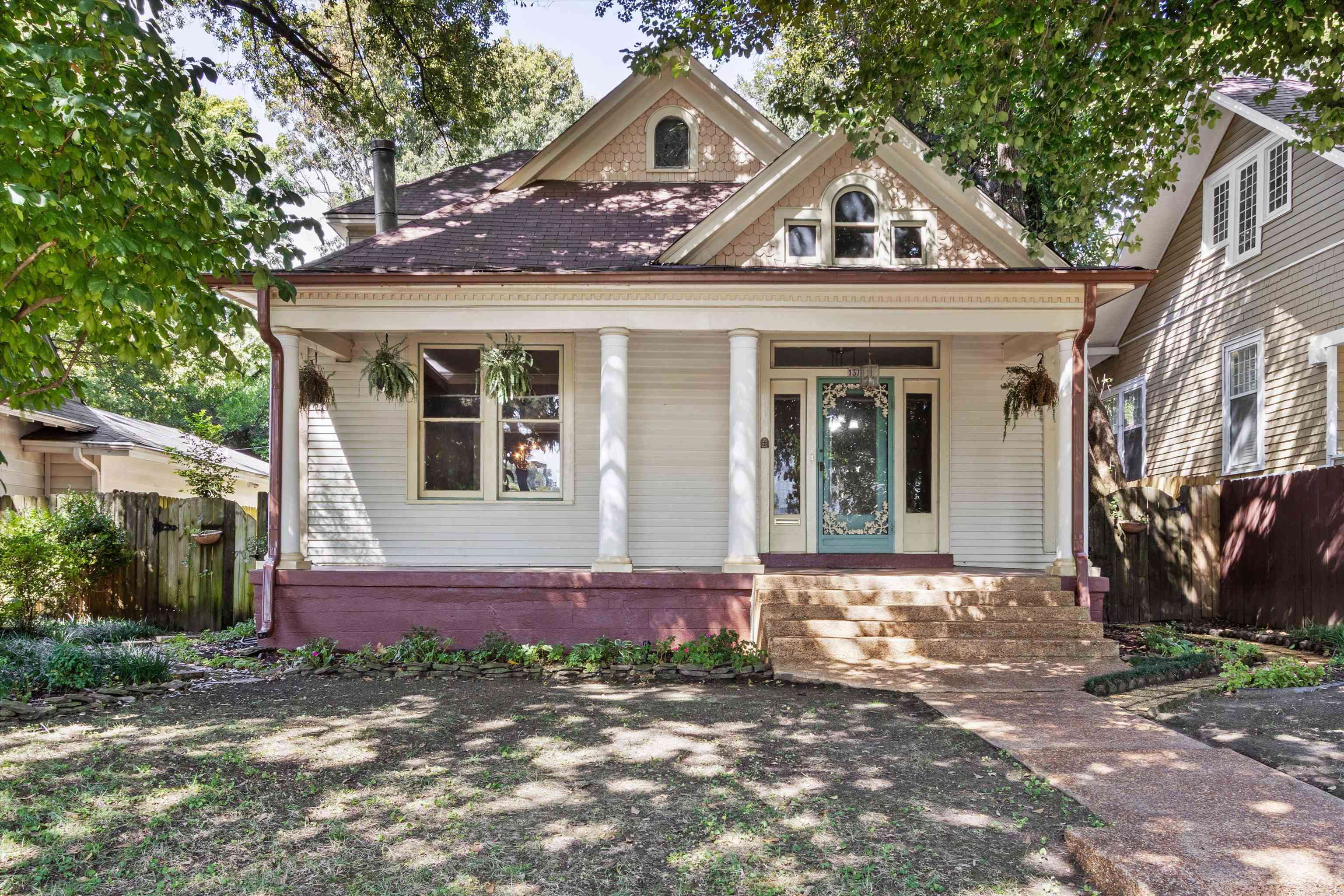 House front with a columned porch, decorative gables, and blue-green door beneath mature trees.