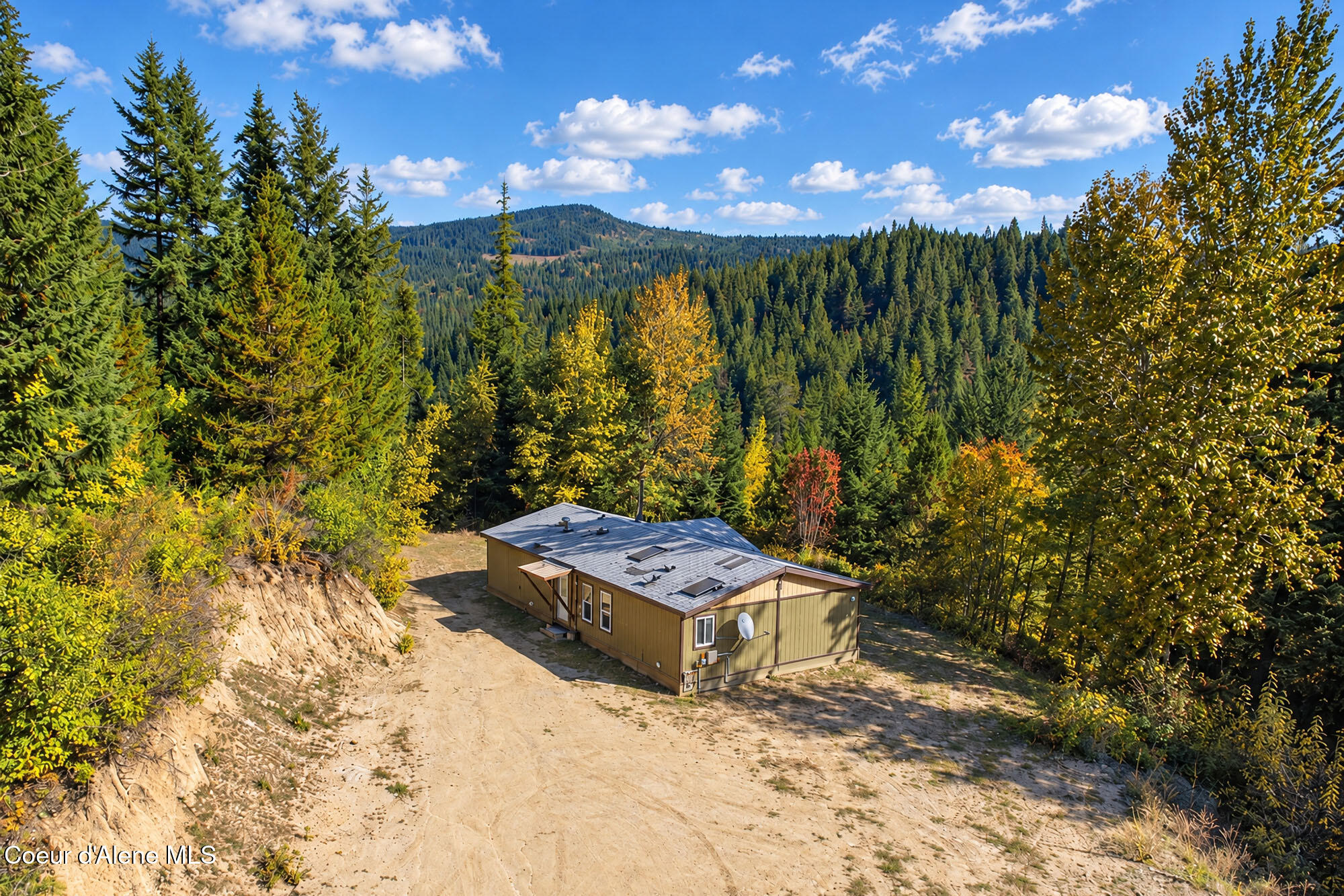 Aerial view of a tan home in a forest clearing, surrounded by evergreens and autumn foliage.