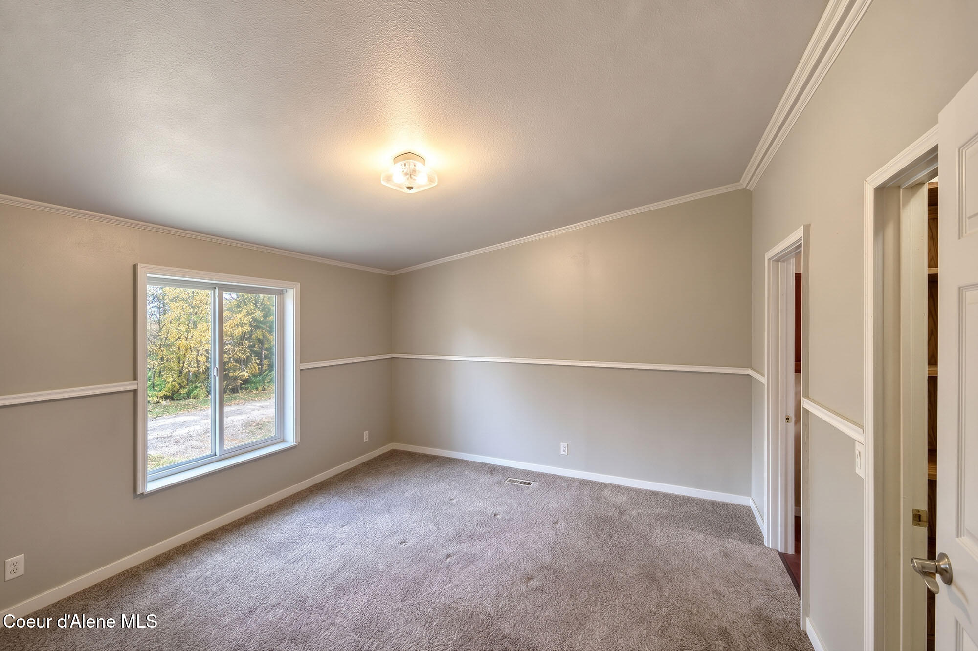 Empty bedroom with gray carpet, a large window, and white-trimmed closet doors.