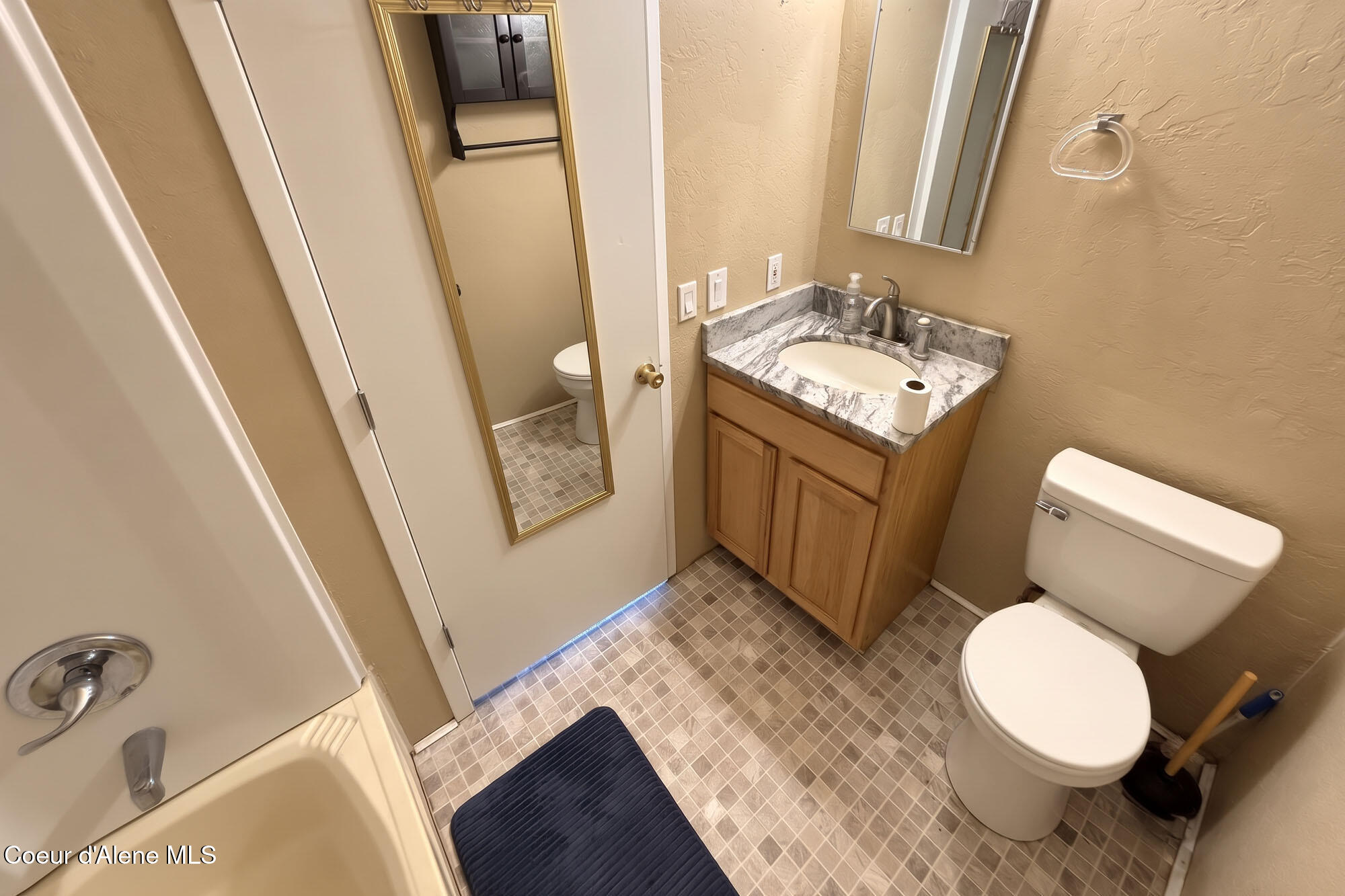 Bathroom with a wood vanity, marble-pattern counter, bathtub, and toilet.