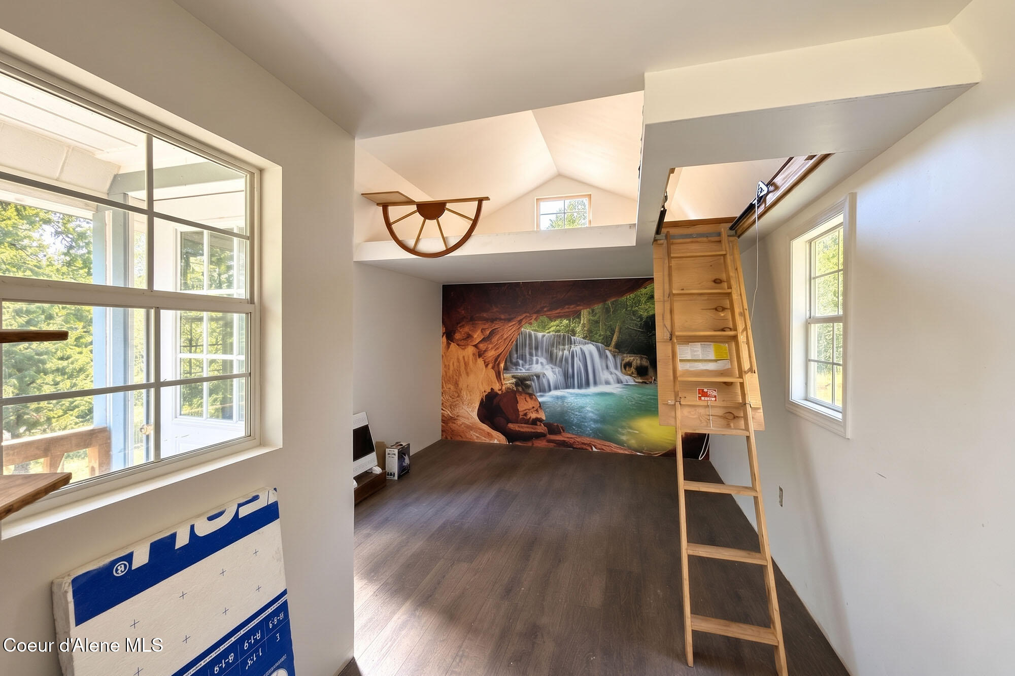 Bright loft room with a wooden ladder, large windows, and a waterfall mural.