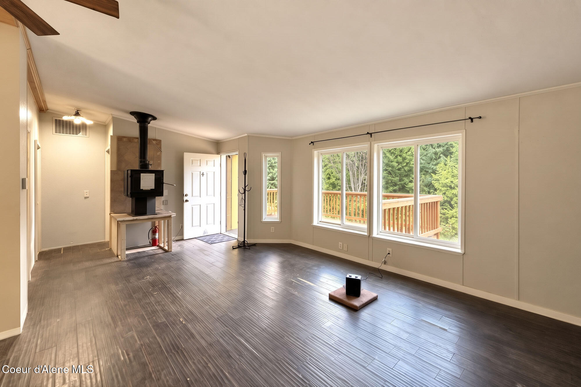 Vacant living room with a wood stove and large windows overlooking a deck and trees.