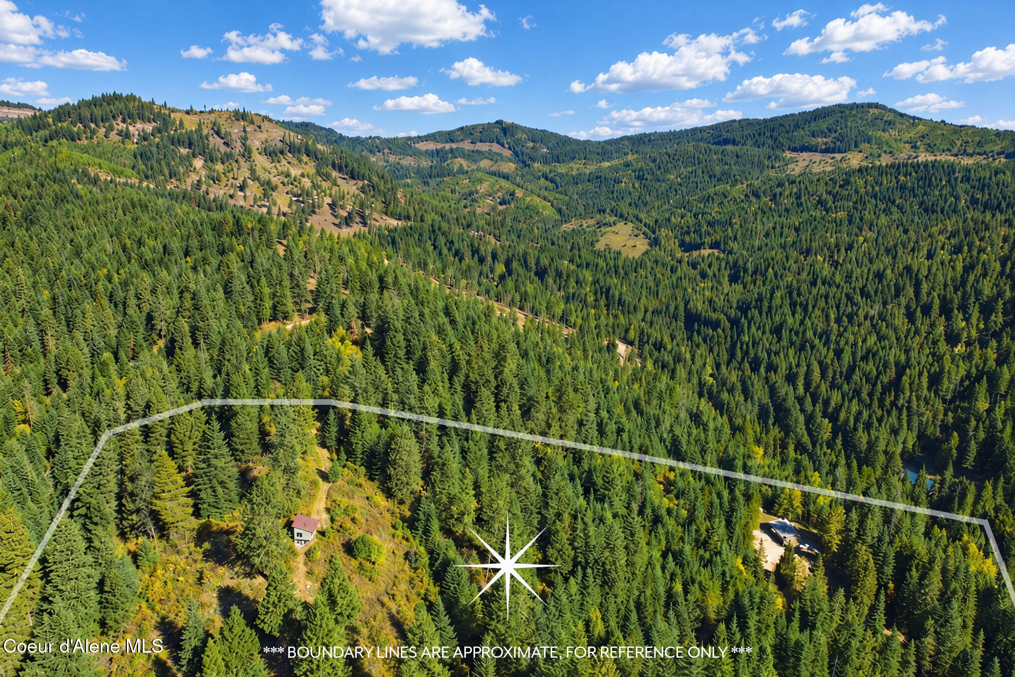 Aerial view of wooded mountain acreage outlined with approximate boundaries, with two buildings among the trees.