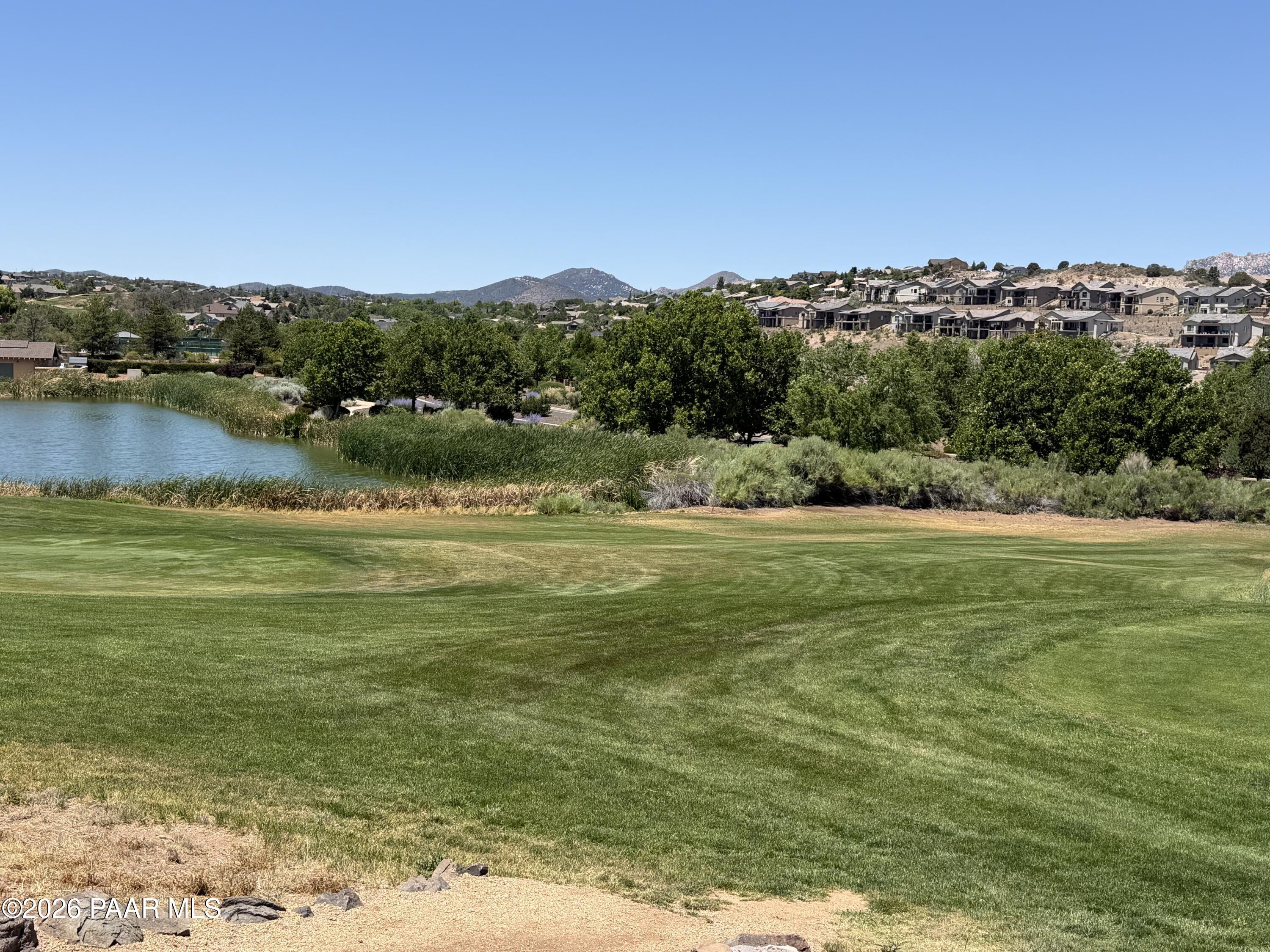 Golf course lawn beside a reed-lined pond, with hillside homes and mountains beyond.