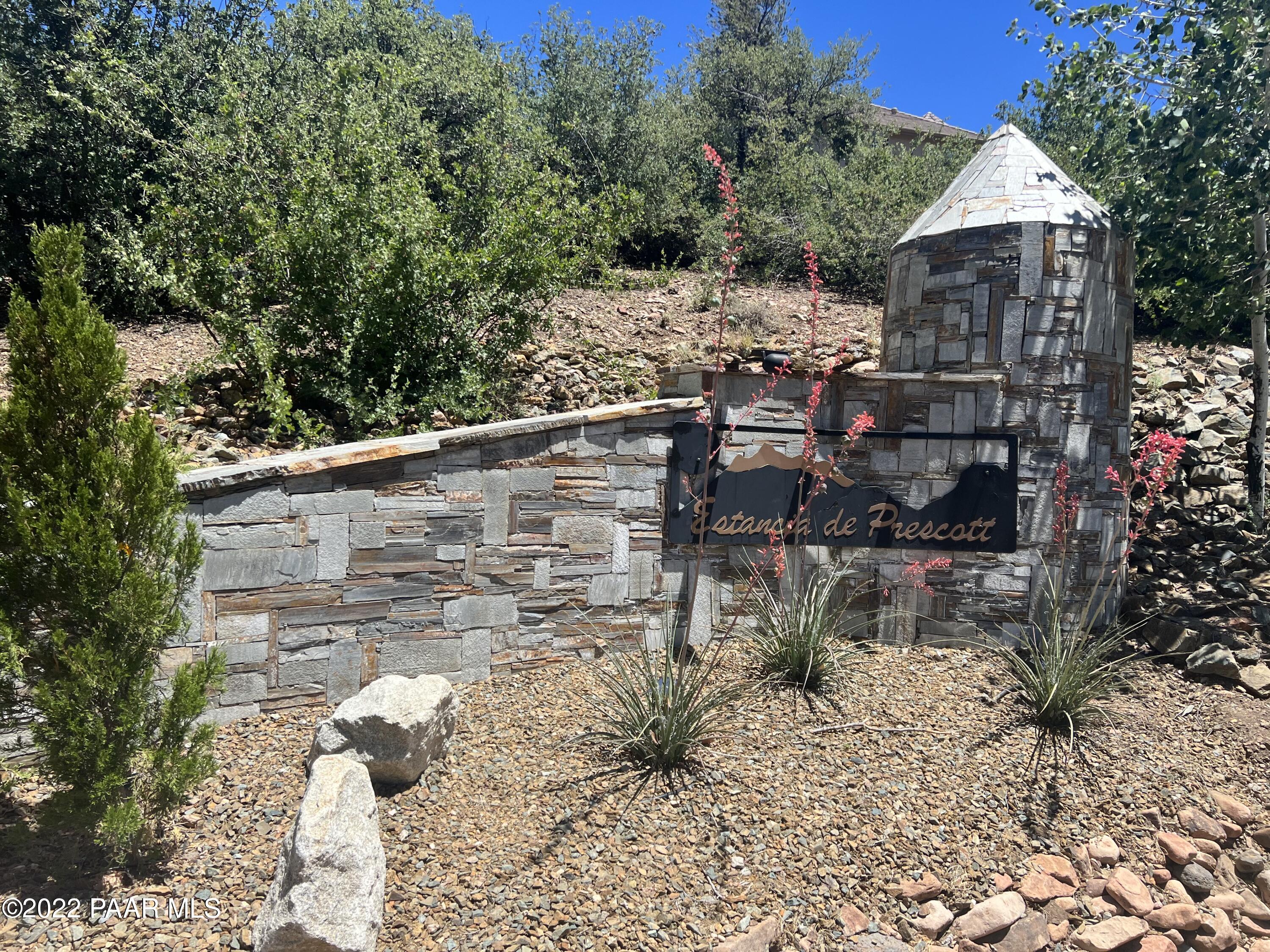 Stone entrance monument for Estancia de Prescott amid rocky landscaping and desert plants.
