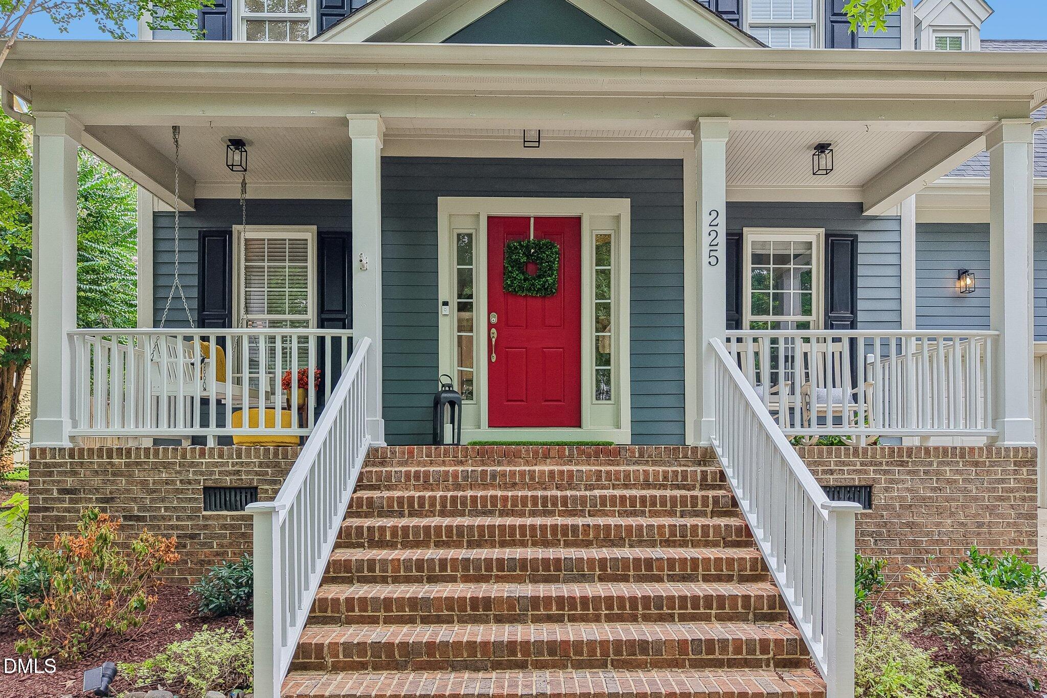 Blue-sided home with a red front door, covered porch, white railings, and wide brick steps.