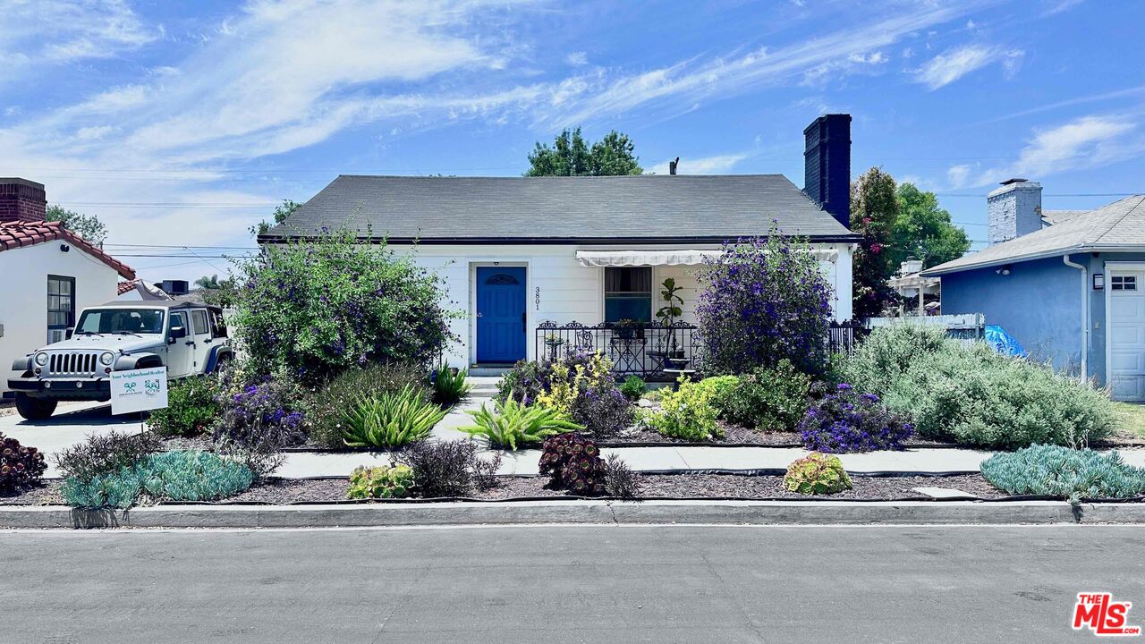 White single-story house with a blue front door, covered porch, and flowering drought-tolerant landscaping.
