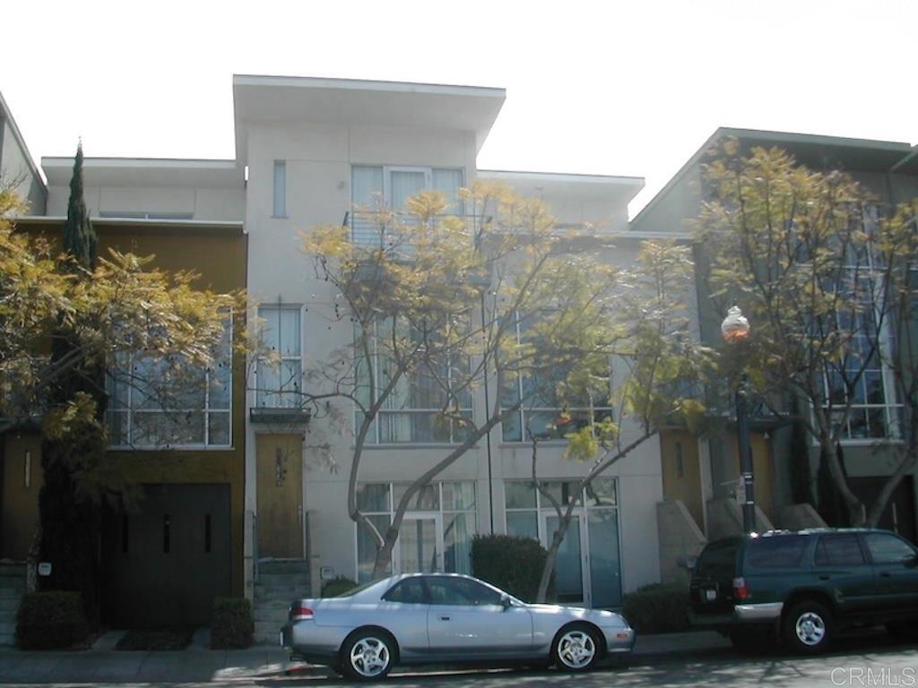 Modern multi-unit building with large windows, leafy trees, and cars parked along the curb.