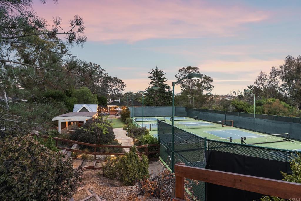 Outdoor tennis courts beside a landscaped garden and pavilion at dusk.