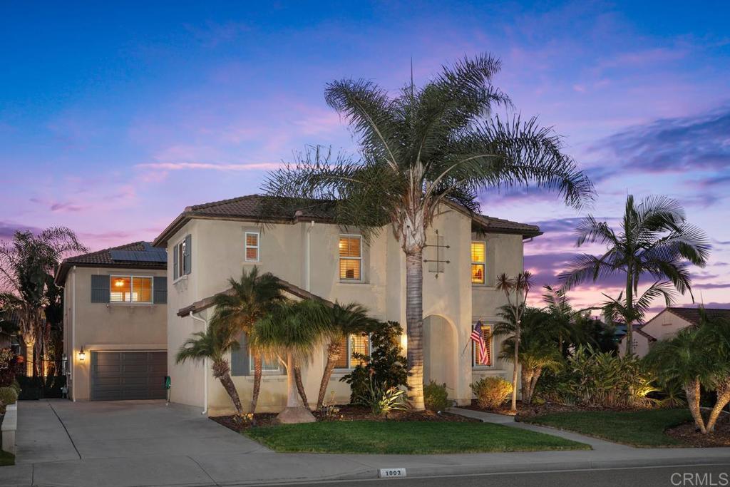 Two-story stucco home with a garage and palm trees, photographed at dusk.