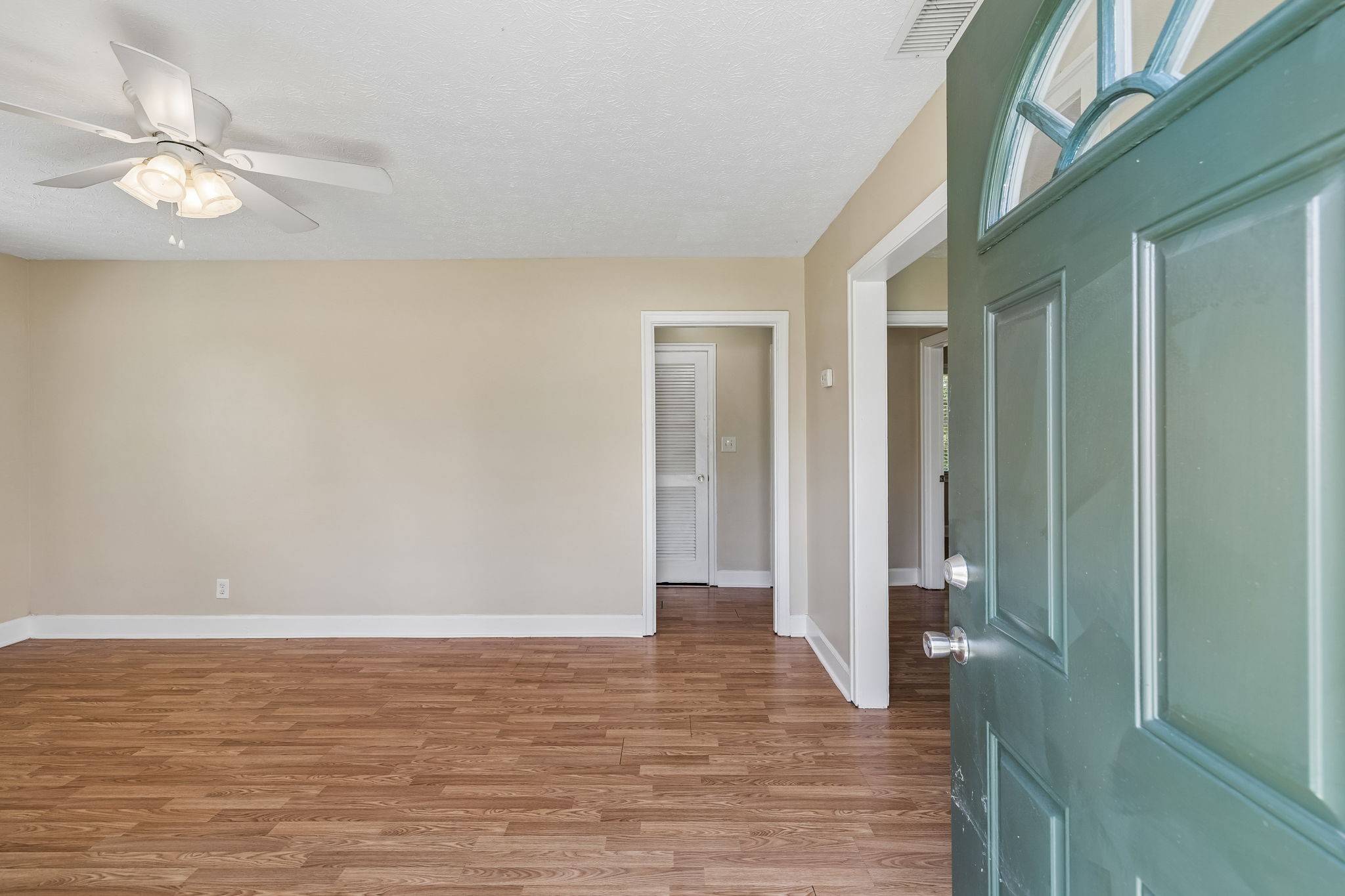 Empty room with wood-look floors and beige walls, viewed past an open green front door.