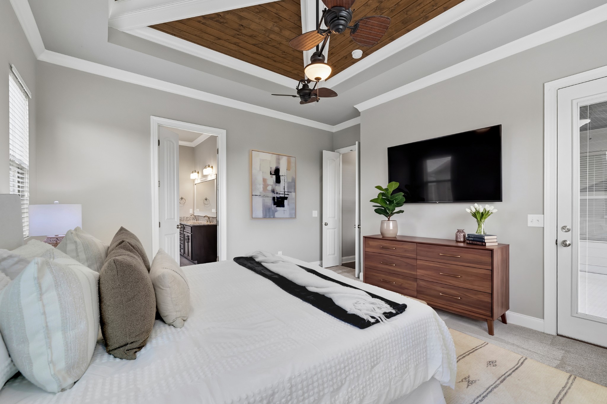 Bedroom with a wood-plank tray ceiling, ceiling fans, and wall-mounted television.