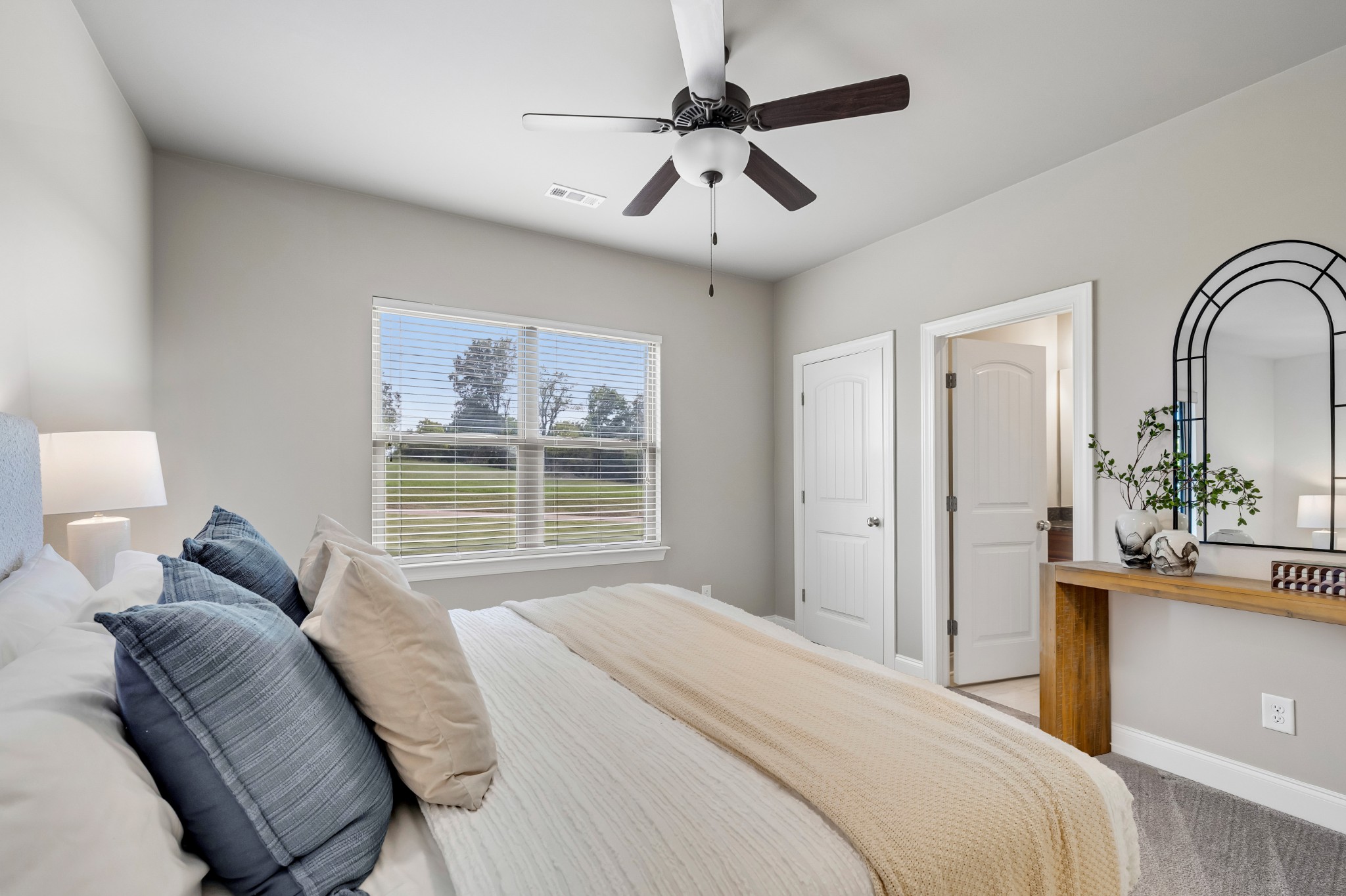 Bedroom with a white bed, blue pillows, a window overlooking a lawn, and a ceiling fan.