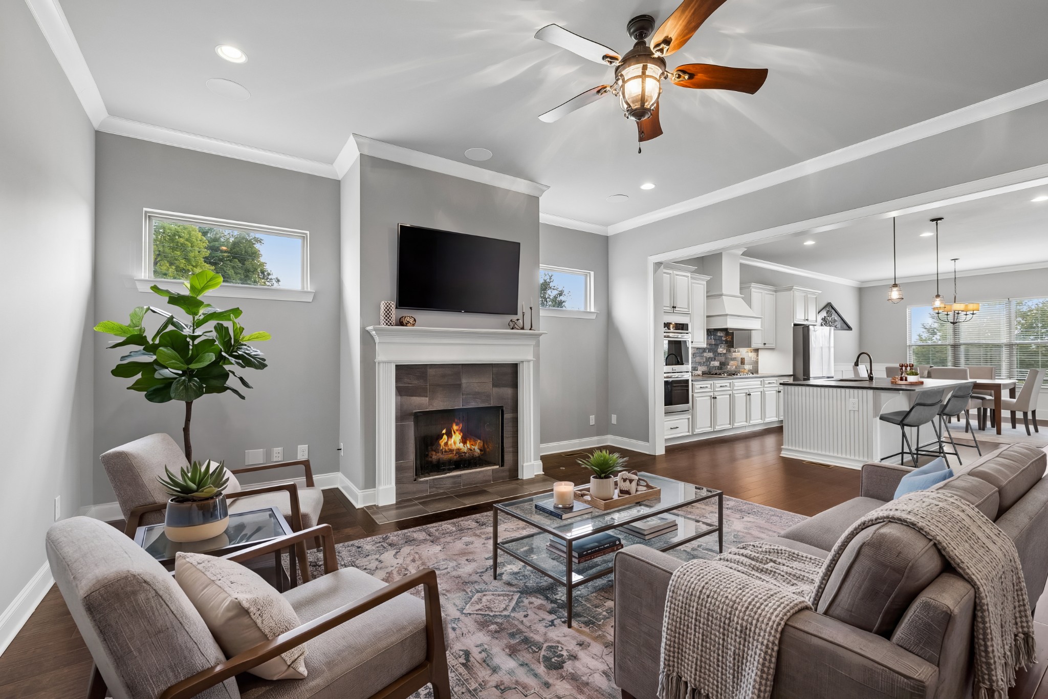 Open-plan living room with a fireplace and television, connected to a bright white kitchen and dining area.