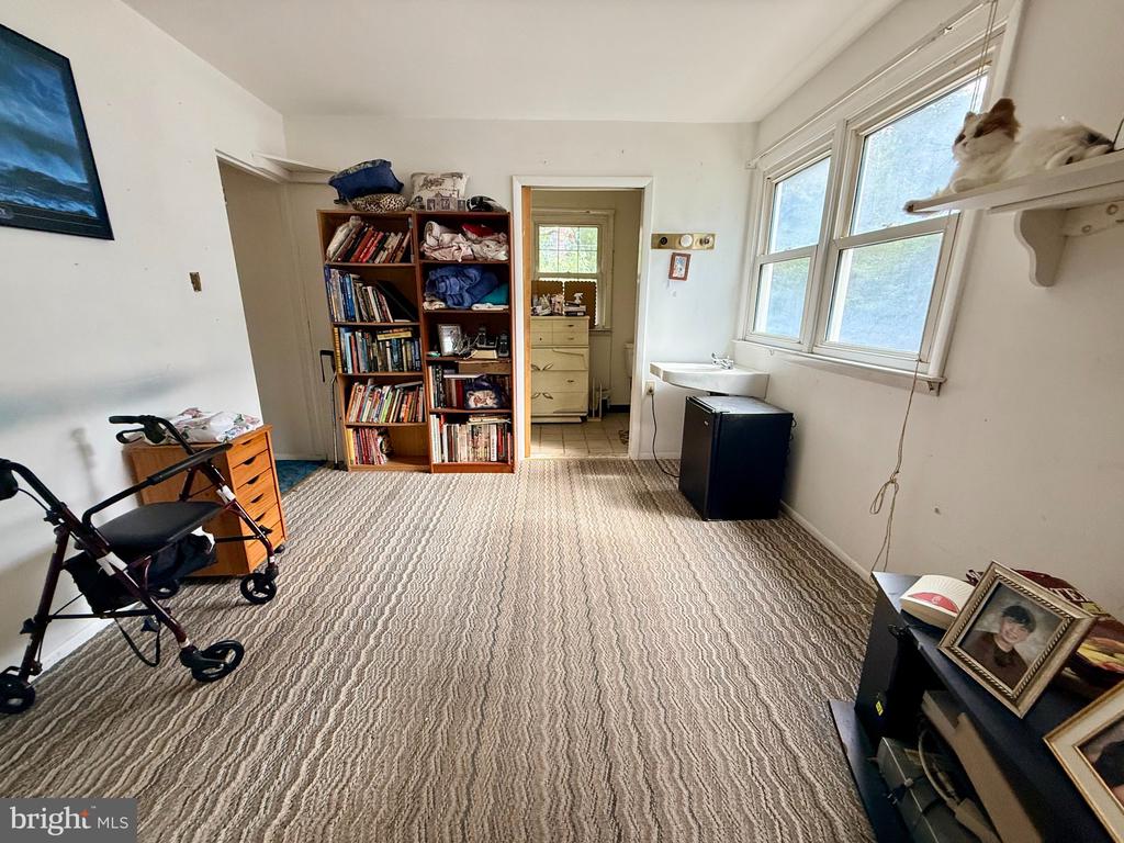 Carpeted room with crowded bookshelves, wide windows, and a small sink.