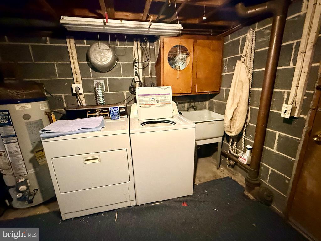 Basement laundry area with a washer, dryer, utility sink, and exposed block walls.