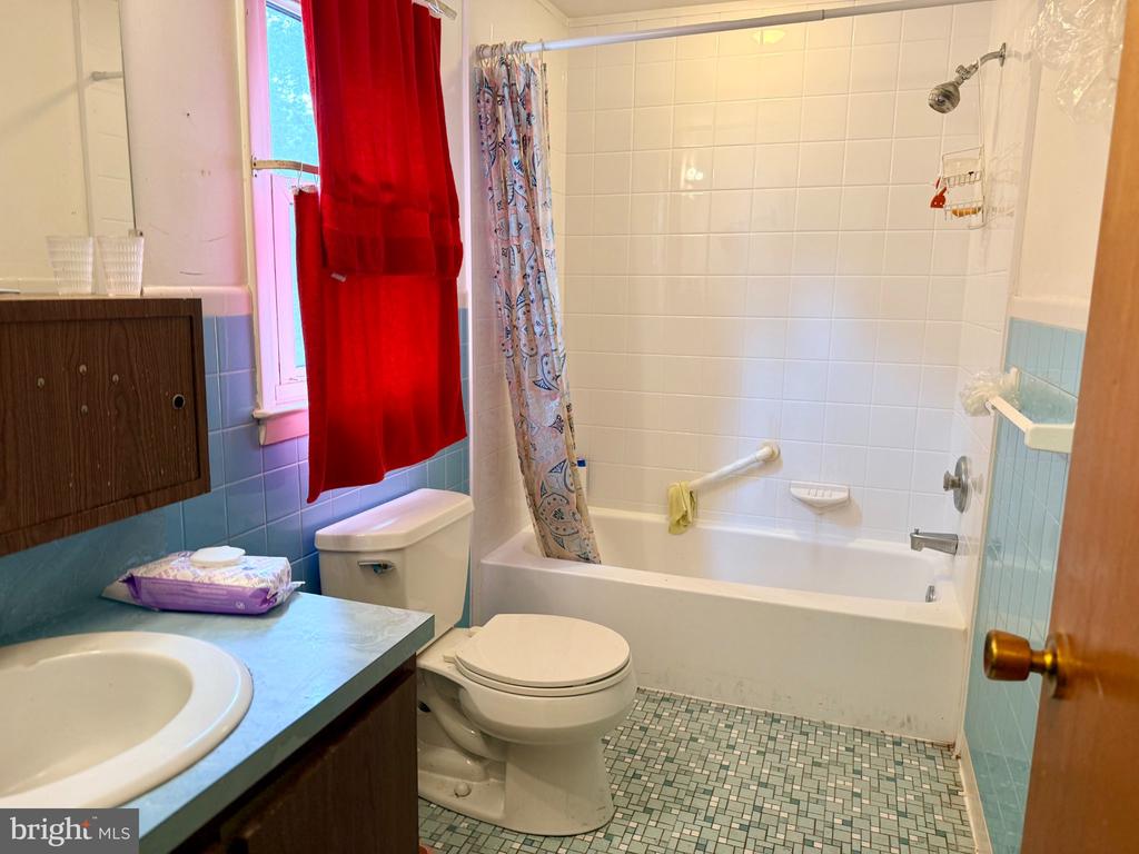 Bathroom with a bathtub, toilet, and blue-tiled vanity; a vivid red curtain covers the window.