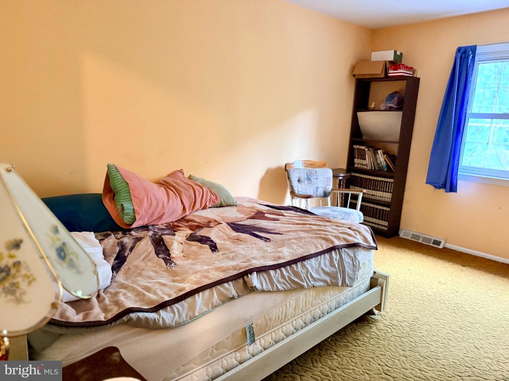 Bedroom with a patterned bedspread, dark bookcase, and blue curtains beside a window.