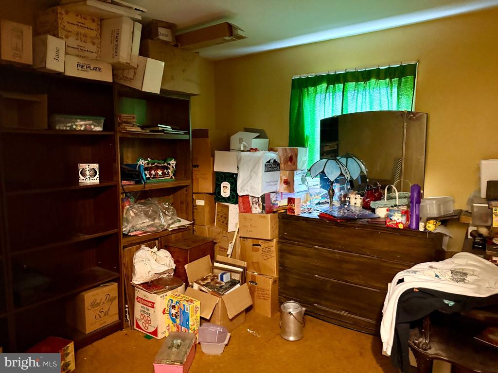 Cluttered bedroom with dark wood shelving, a dresser, boxes, and green curtains.