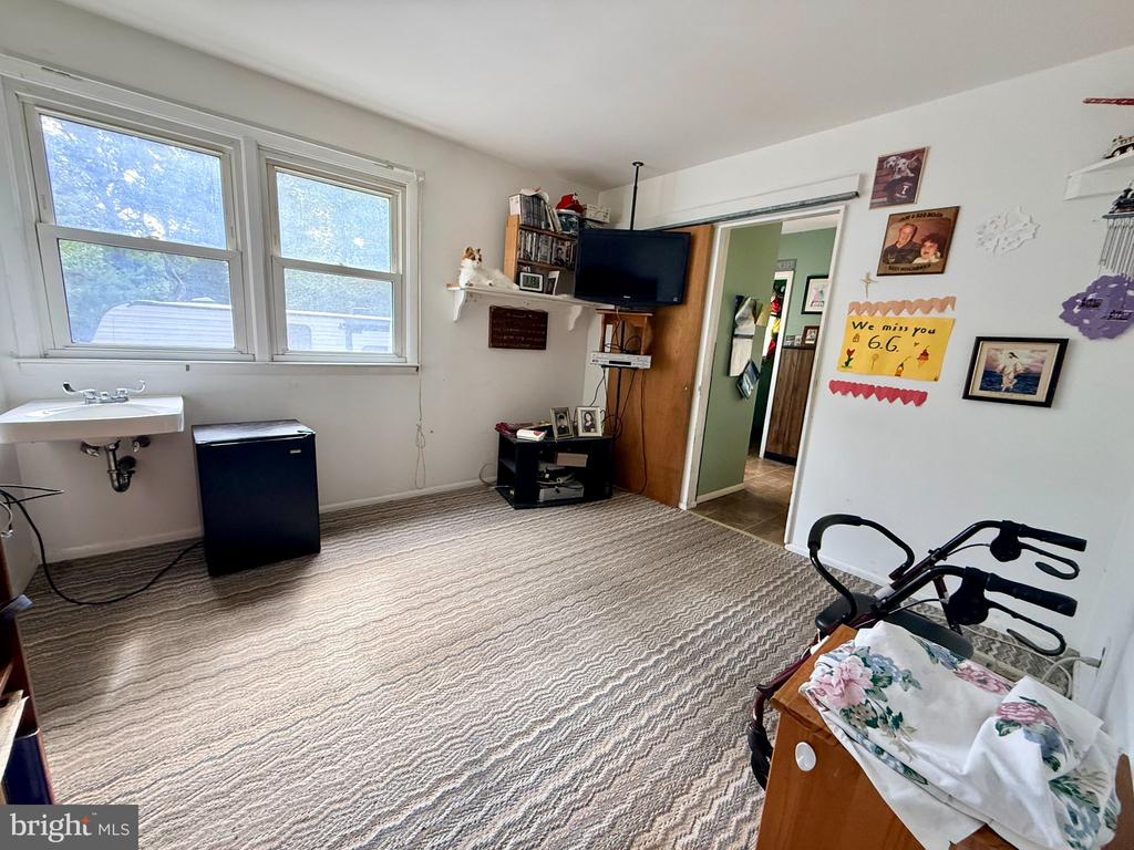 Furnished room with large windows, patterned carpet, a wall-mounted TV, and a small sink.