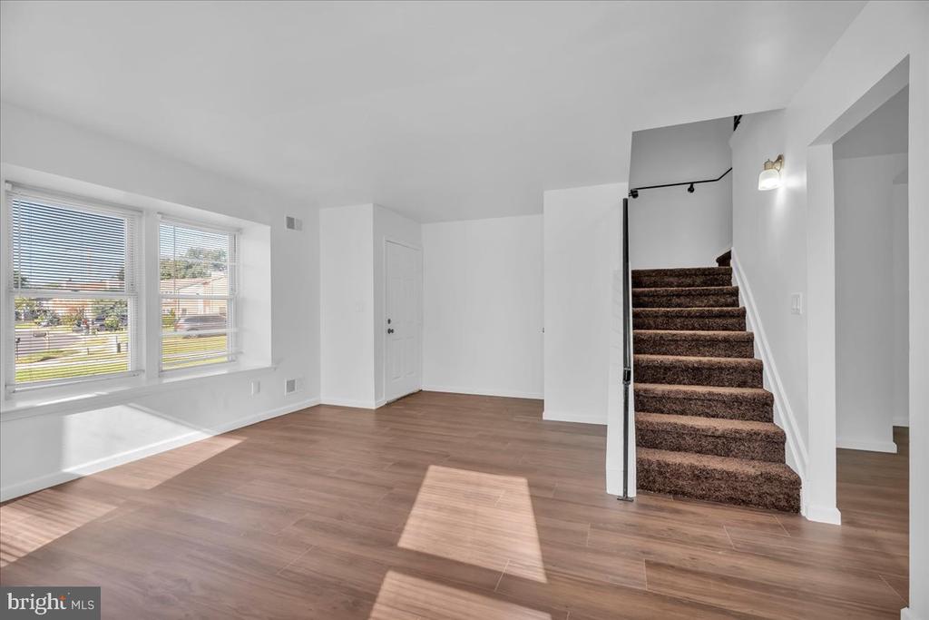 Vacant room with wood-look flooring, two windows, and a carpeted staircase with black railing.