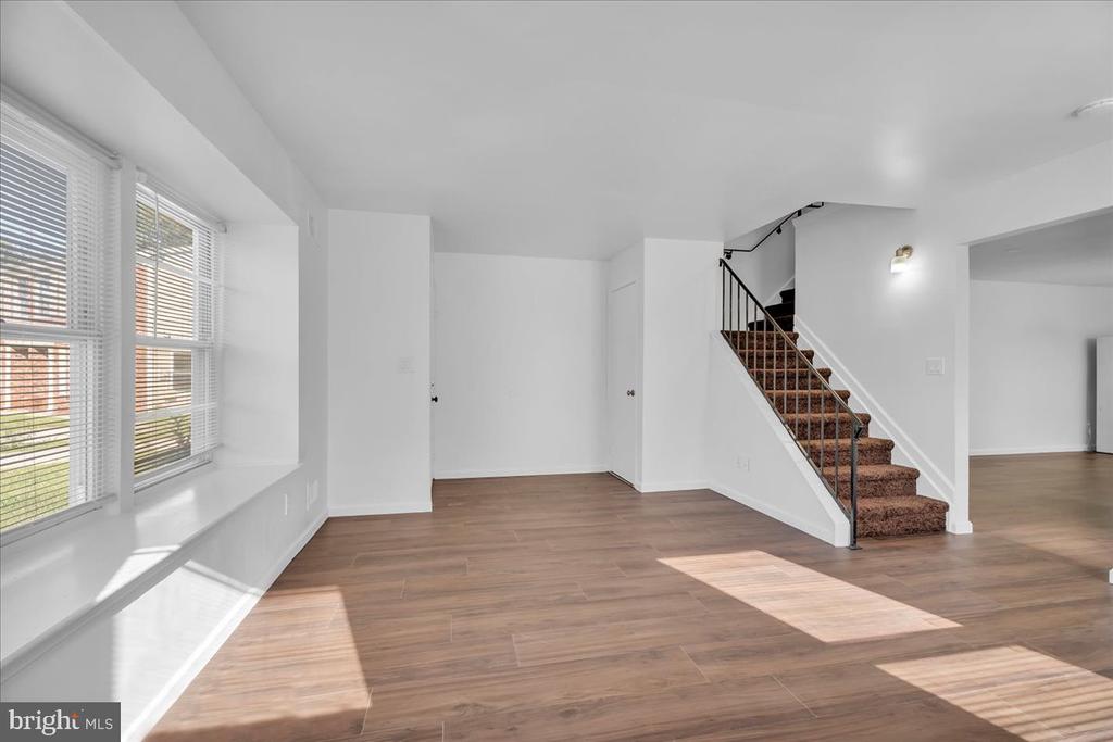 Vacant living area with wood-look flooring, large windows, and a carpeted staircase.