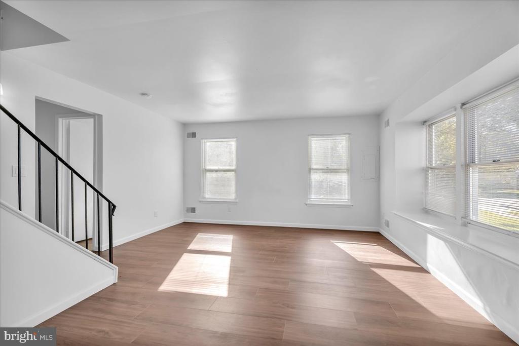 Vacant living room with wood flooring, a black-railed staircase, and large sunlit windows.
