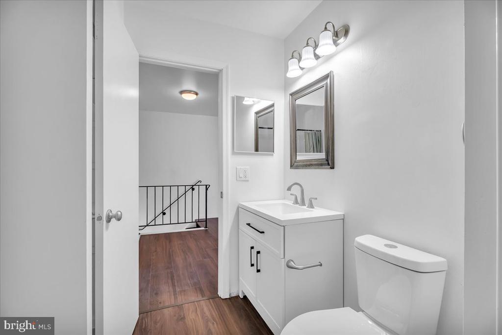 Bathroom with white vanity, toilet, and mirror; doorway opens to a hall with wood-look flooring.