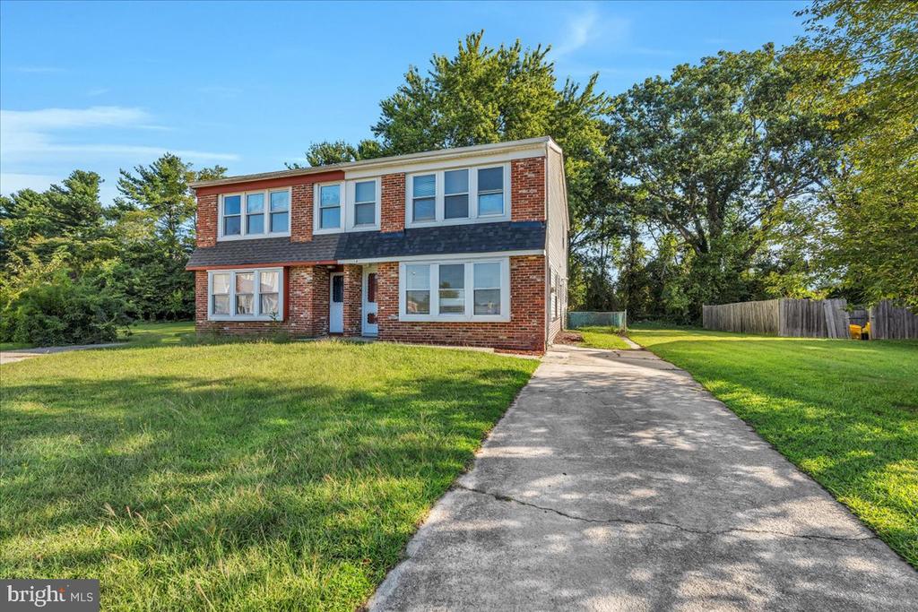 Two-story brick house with a blue front door, broad lawn, and concrete driveway.
